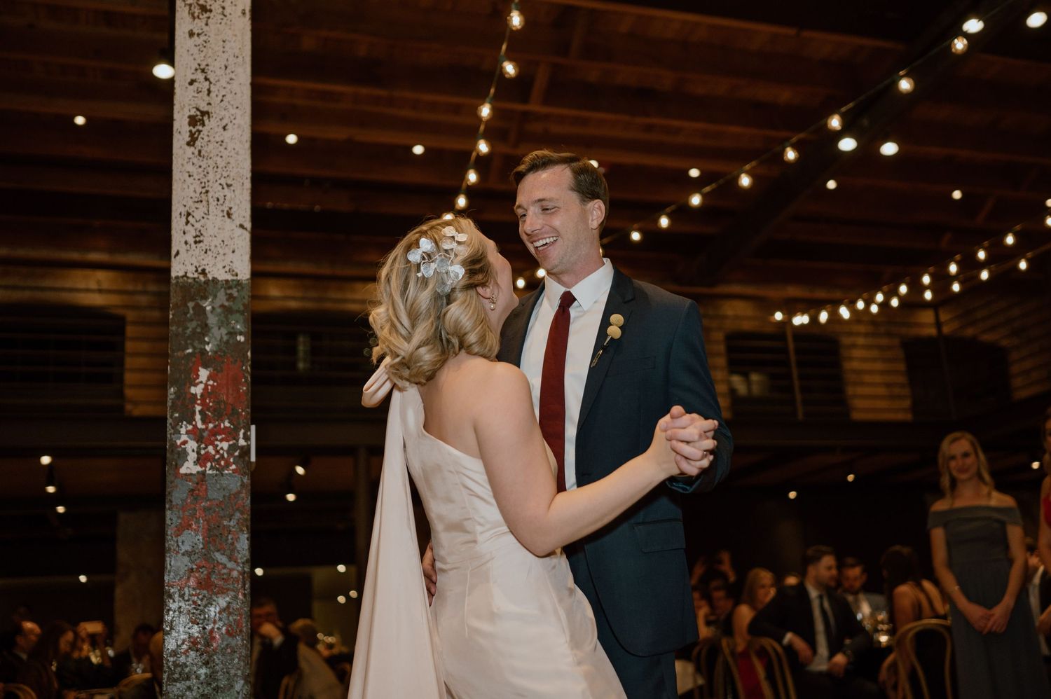 Couple sharing a dance moment under warm string lights in a rustic venue.