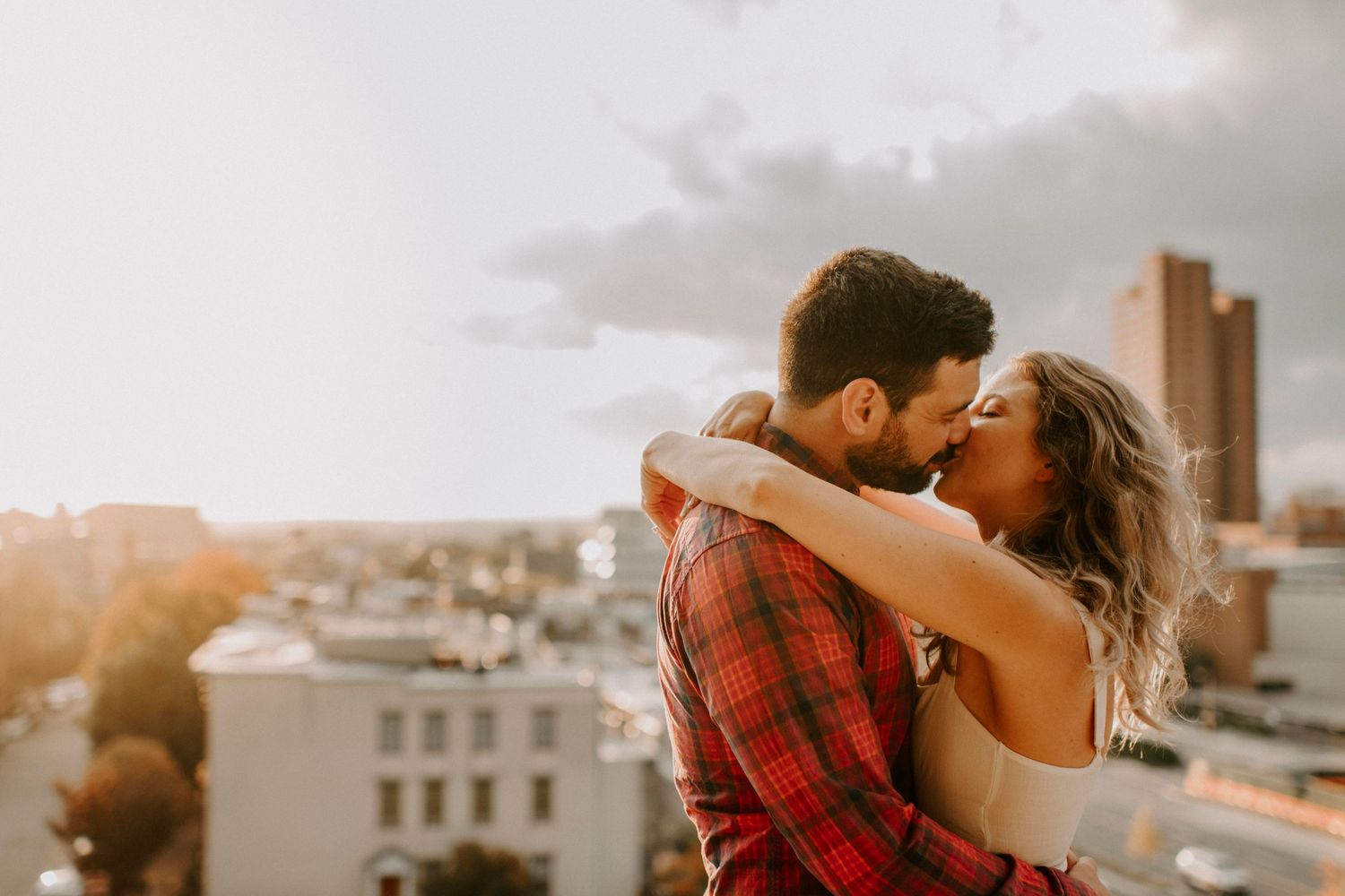 Couple sharing intimate moment on rooftop with golden sunset and cityscape backdrop.