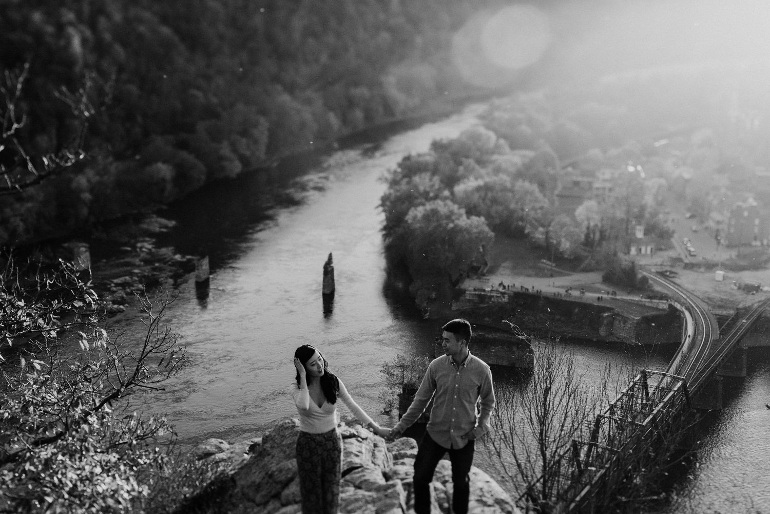 Black and white landscape photo of couple viewing river valley from rocky overlook.