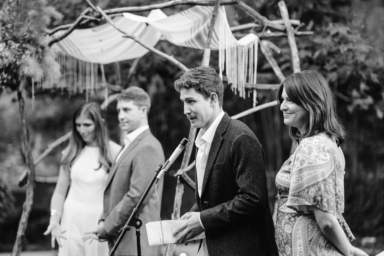Black and white photo of a wedding ceremony under a handmade canopy with hanging decorations.