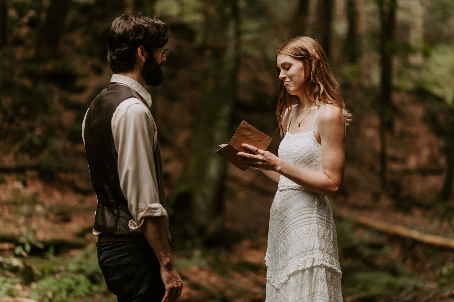 A wedding ceremony takes place in a wooded forest setting with two people exchanging vows.