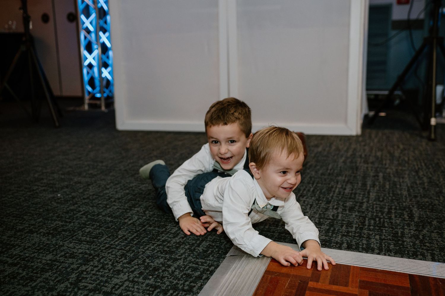 Two young boys in white shirts playing on carpeted floor.