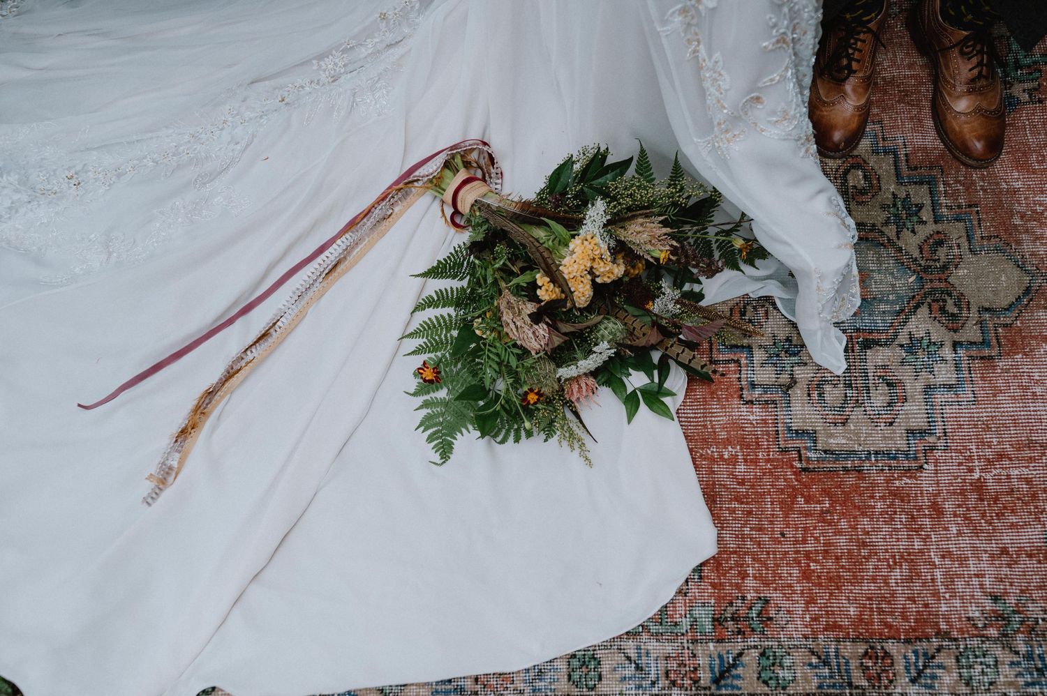 Close-up of a bridal bouquet with ferns and flowers laying on white fabric.