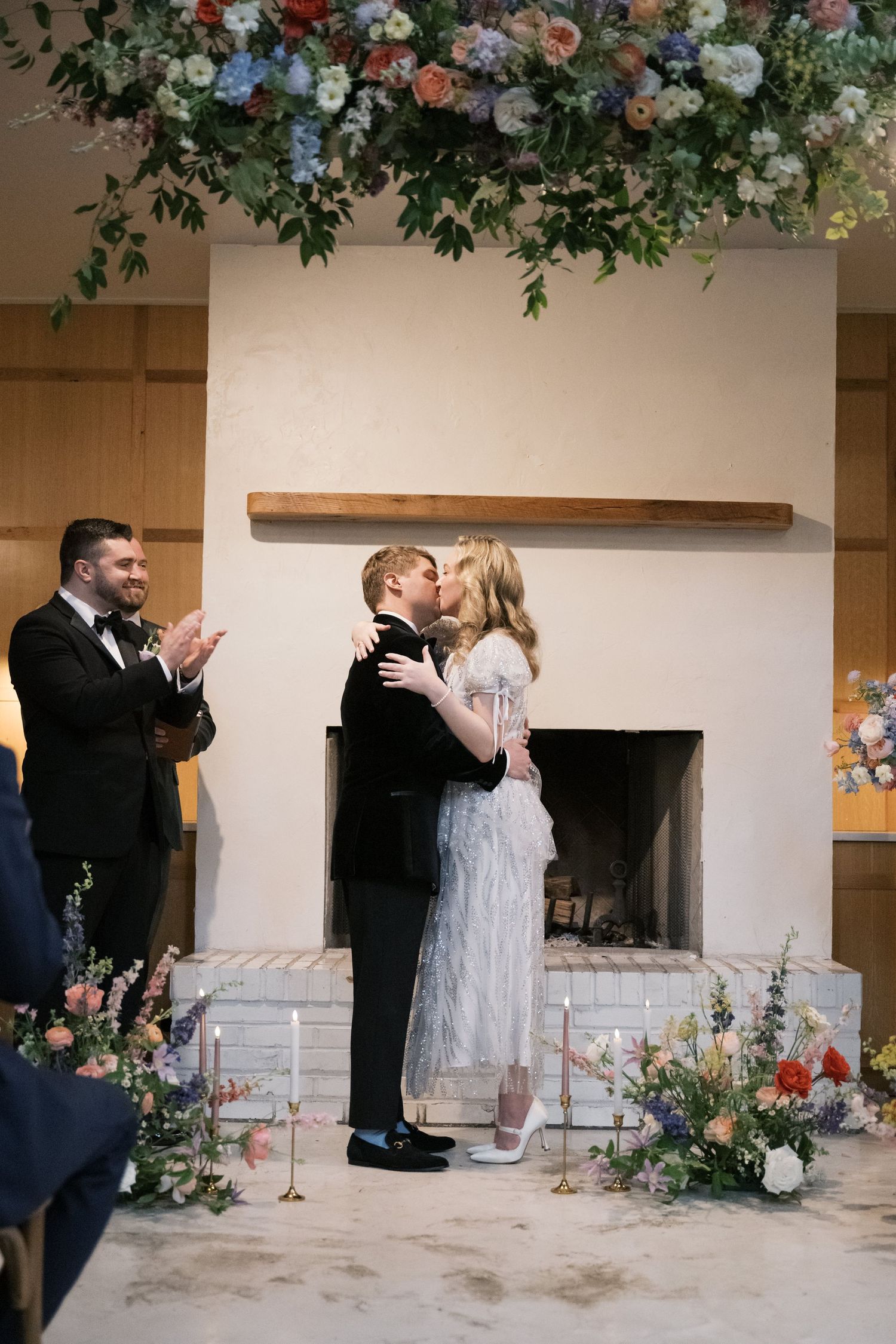 First kiss as newlyweds under floral arch with guests applauding.