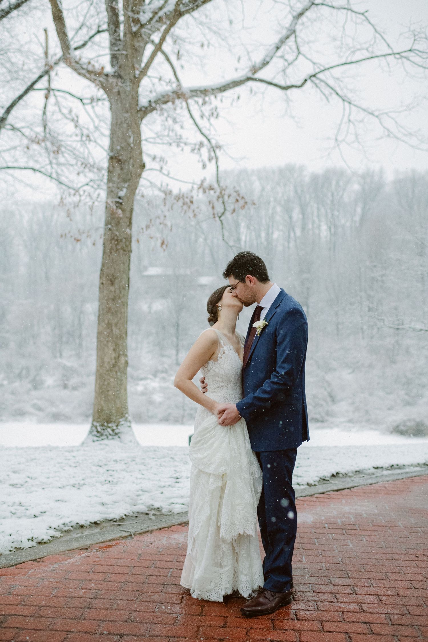 Newlyweds share a tender moment on a snowy winter day on red brick pathway.