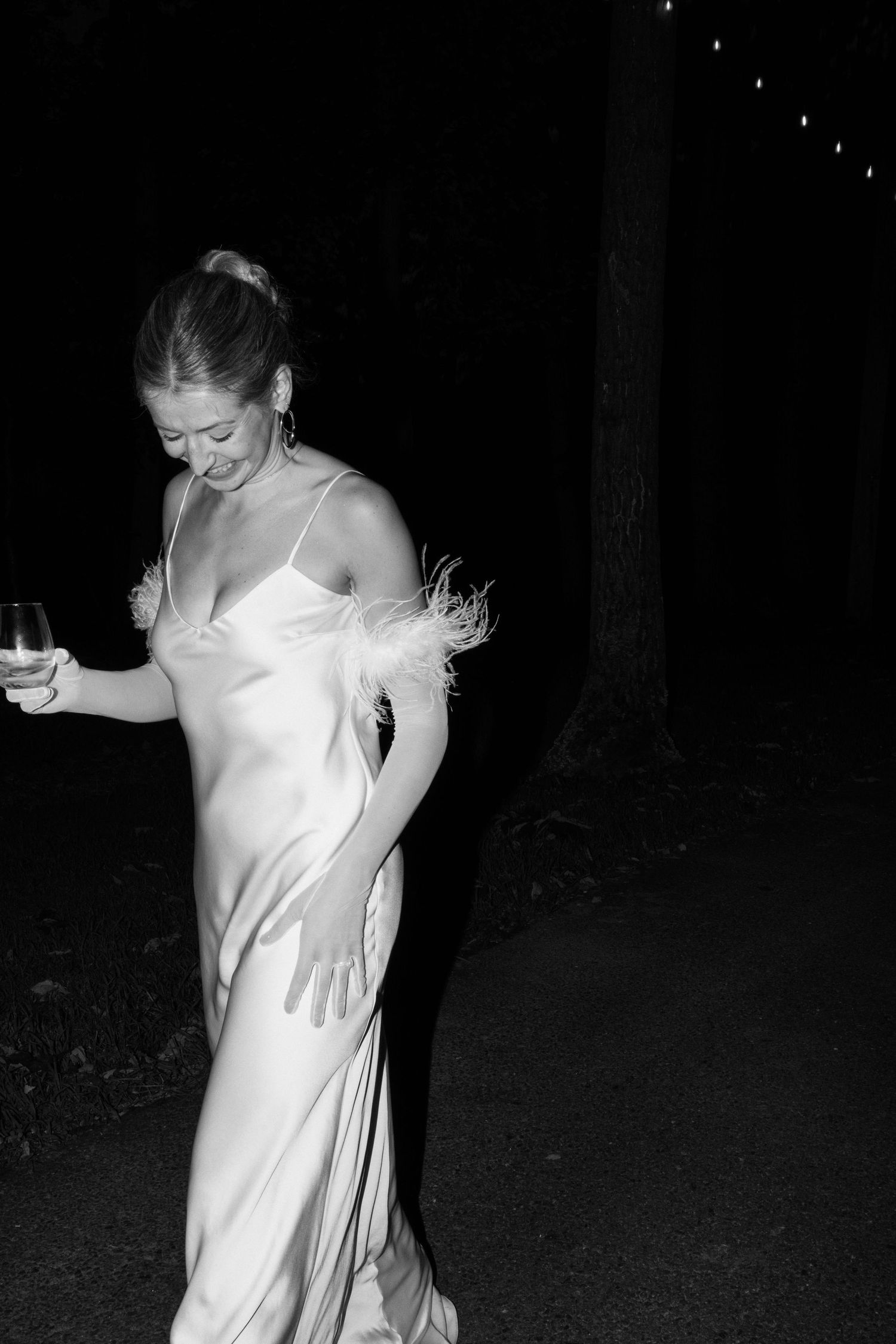 Black and white photo of bride dancing in a silk slip dress with feather details.