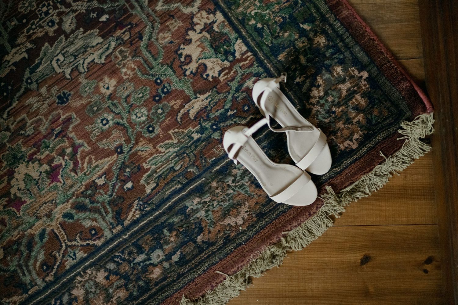 White bridal sandals displayed on ornate vintage rug with intricate floral pattern.