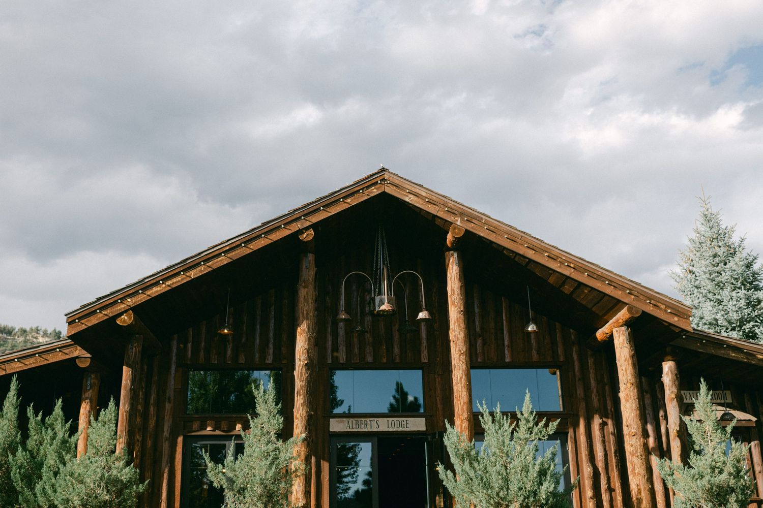 Rustic wooden lodge exterior with large windows and timber beams against cloudy sky.