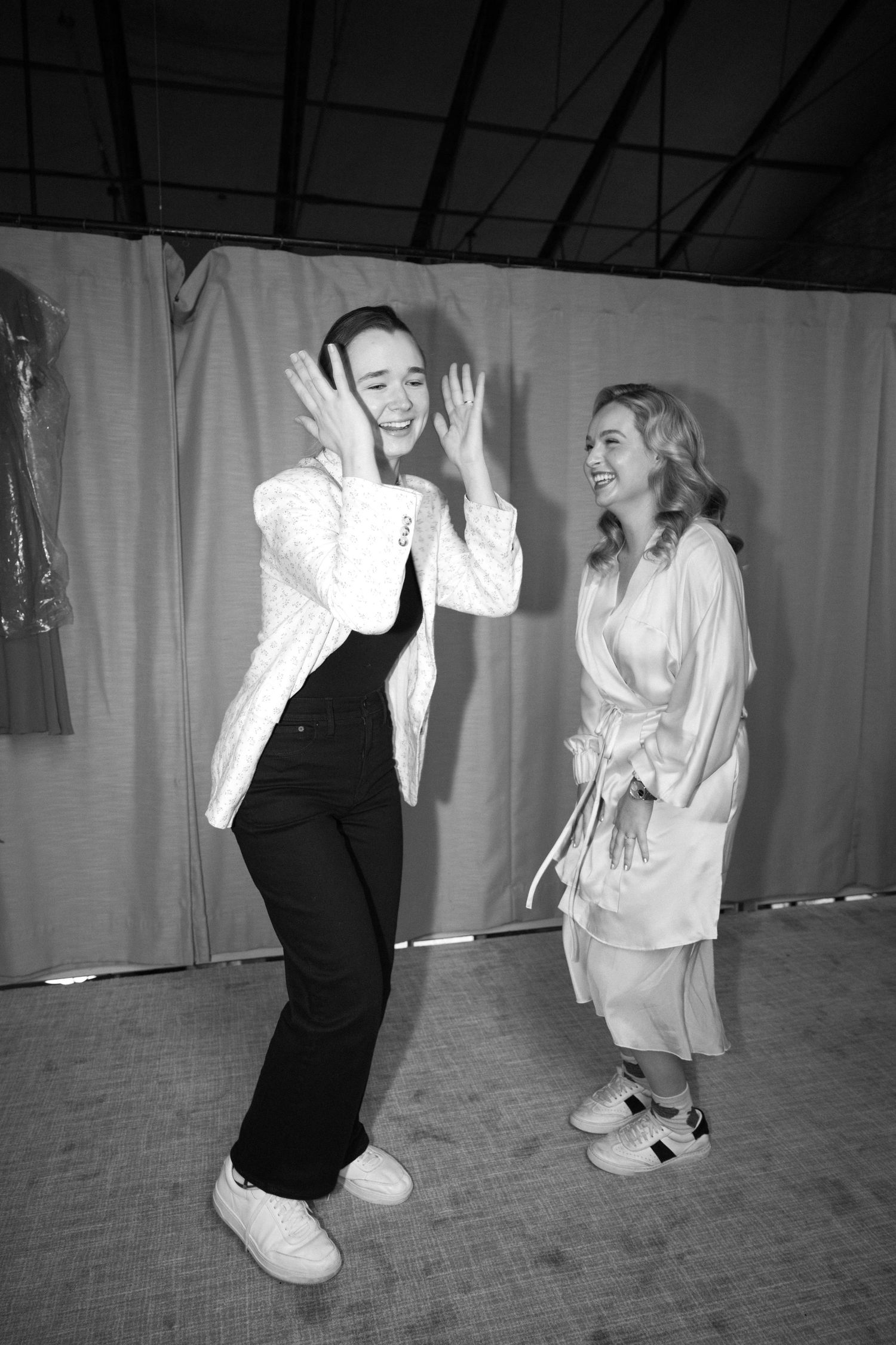 Two people in black and white attire share an energetic dance moment during wedding preparations.