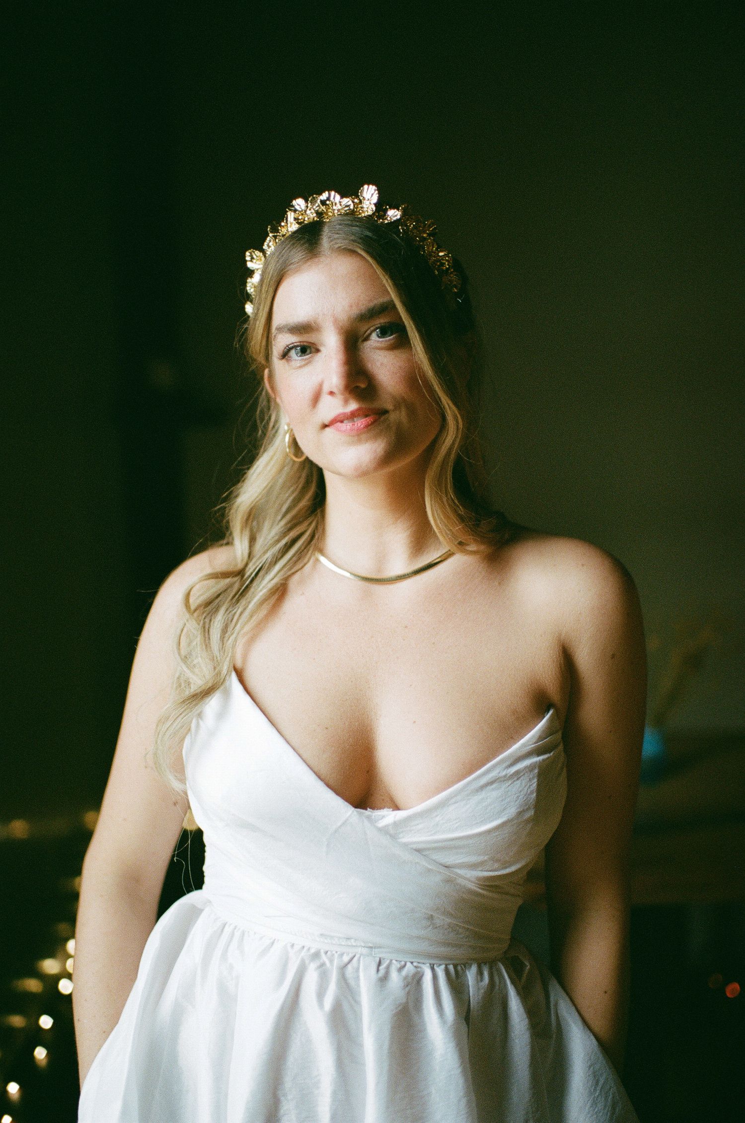 Bride in white strapless wedding dress wearing floral crown and delicate necklace against dark background at Fadensonnen in Baltimore