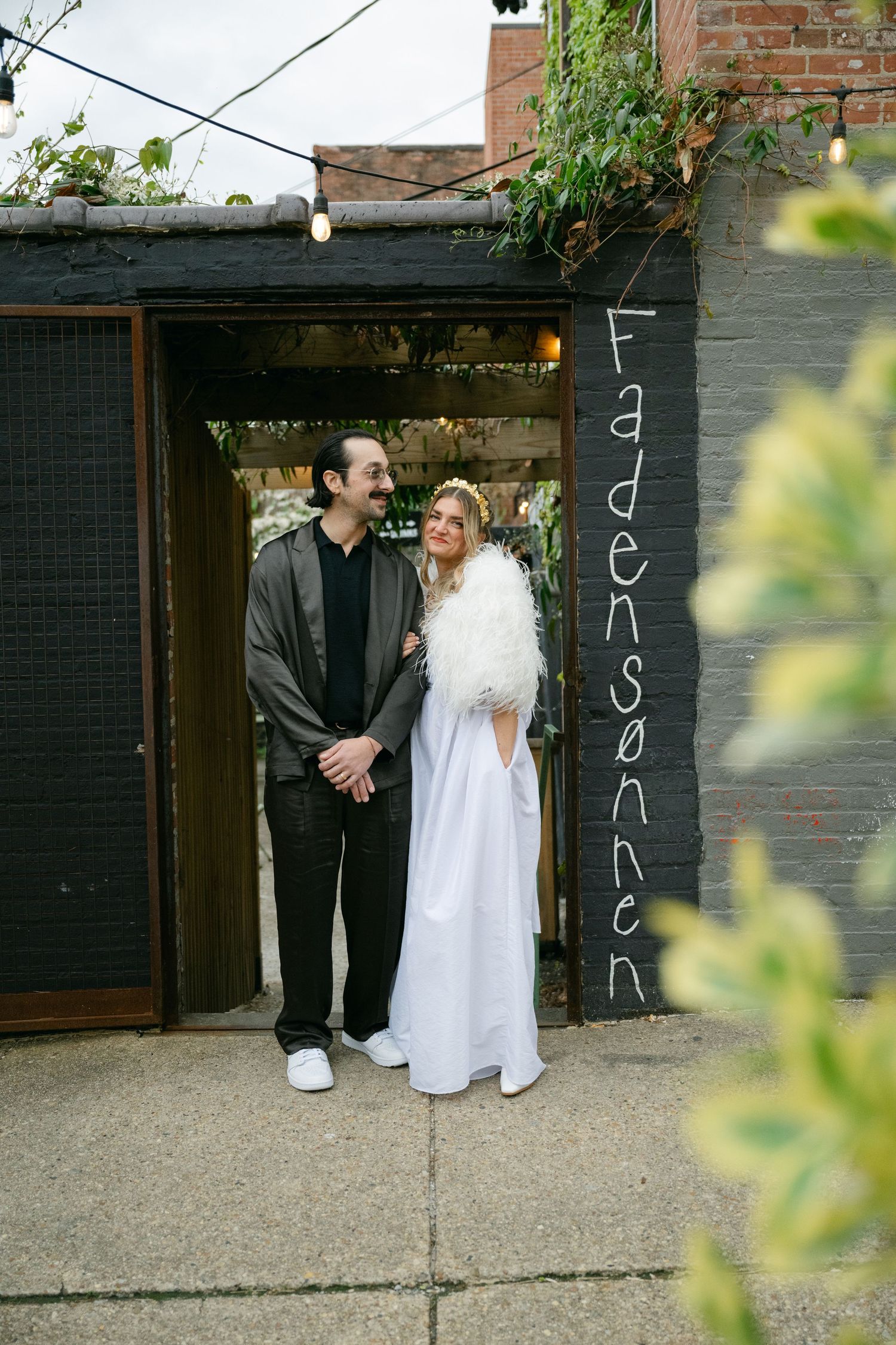 A couple stands outside a brick building with the word 'Fadensonnen' written on the wall at Fadensonnen in Baltimore