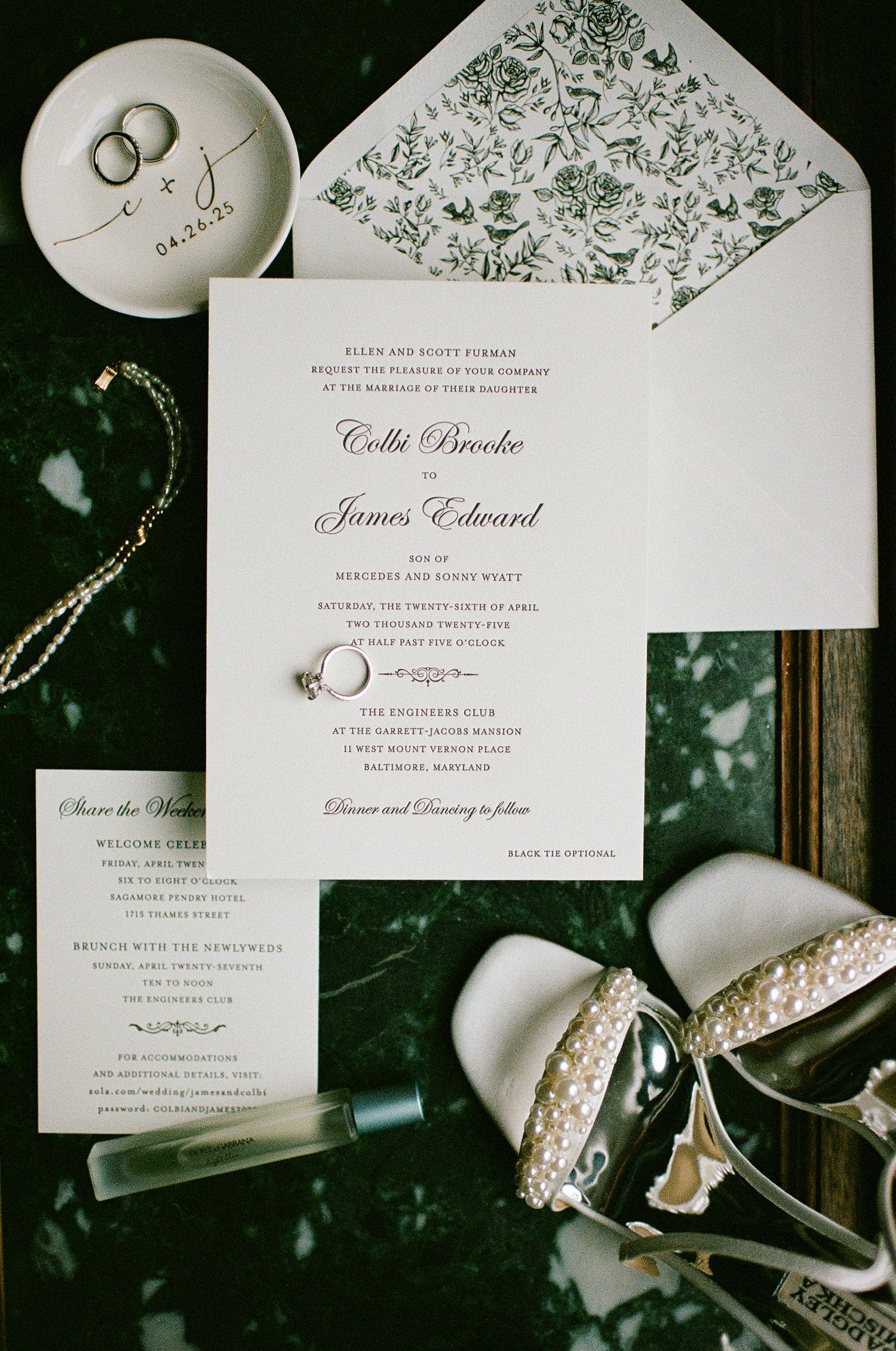 Elegant wedding invitation suite with delicate green floral details and traditional script typography laid out on dark surface.