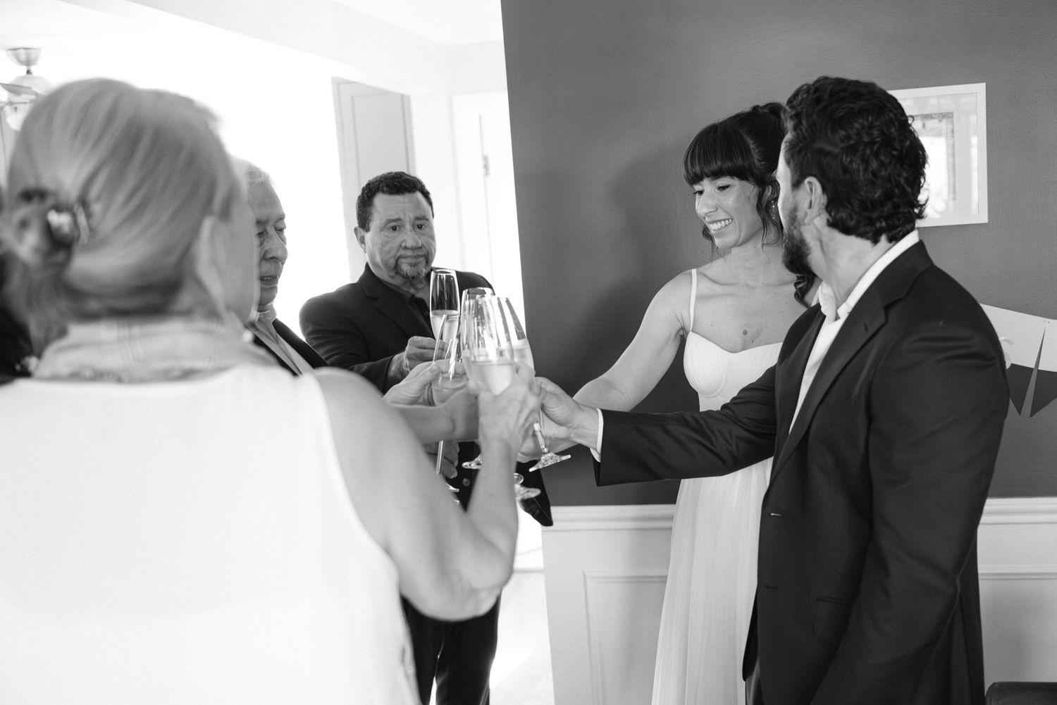 A small group celebrates with champagne glasses during a wedding reception in a light-filled room.