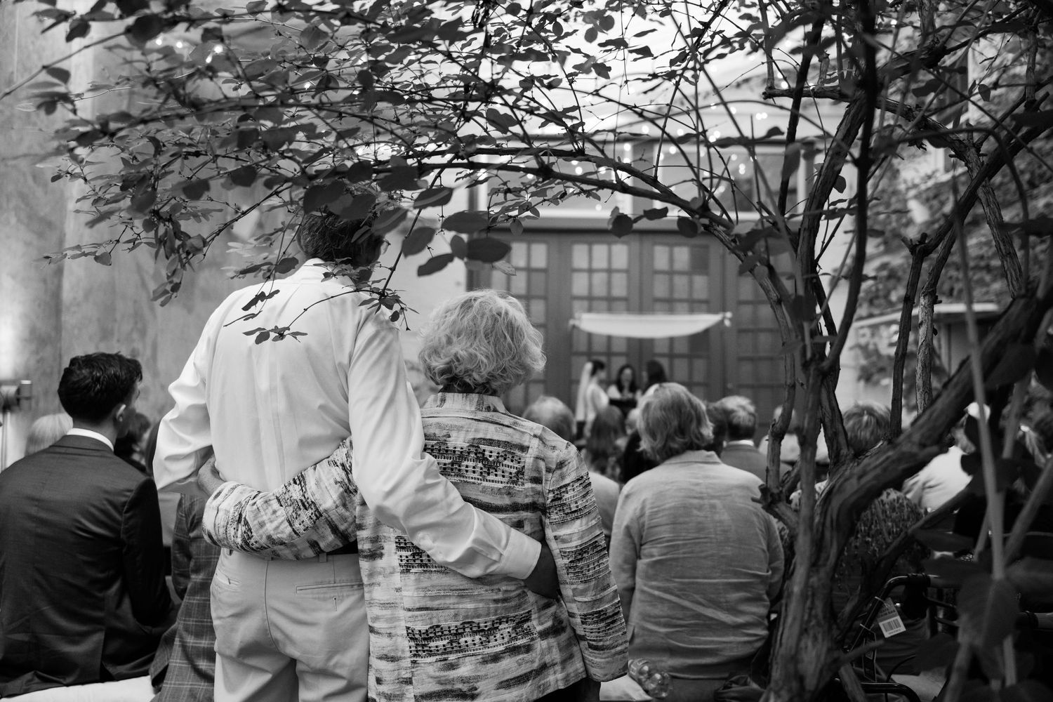 Black and white image of outdoor wedding ceremony guests under trees.