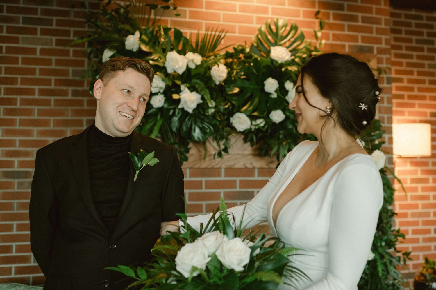 Couple sharing emotional moment in front of floral wall during wedding ceremony.