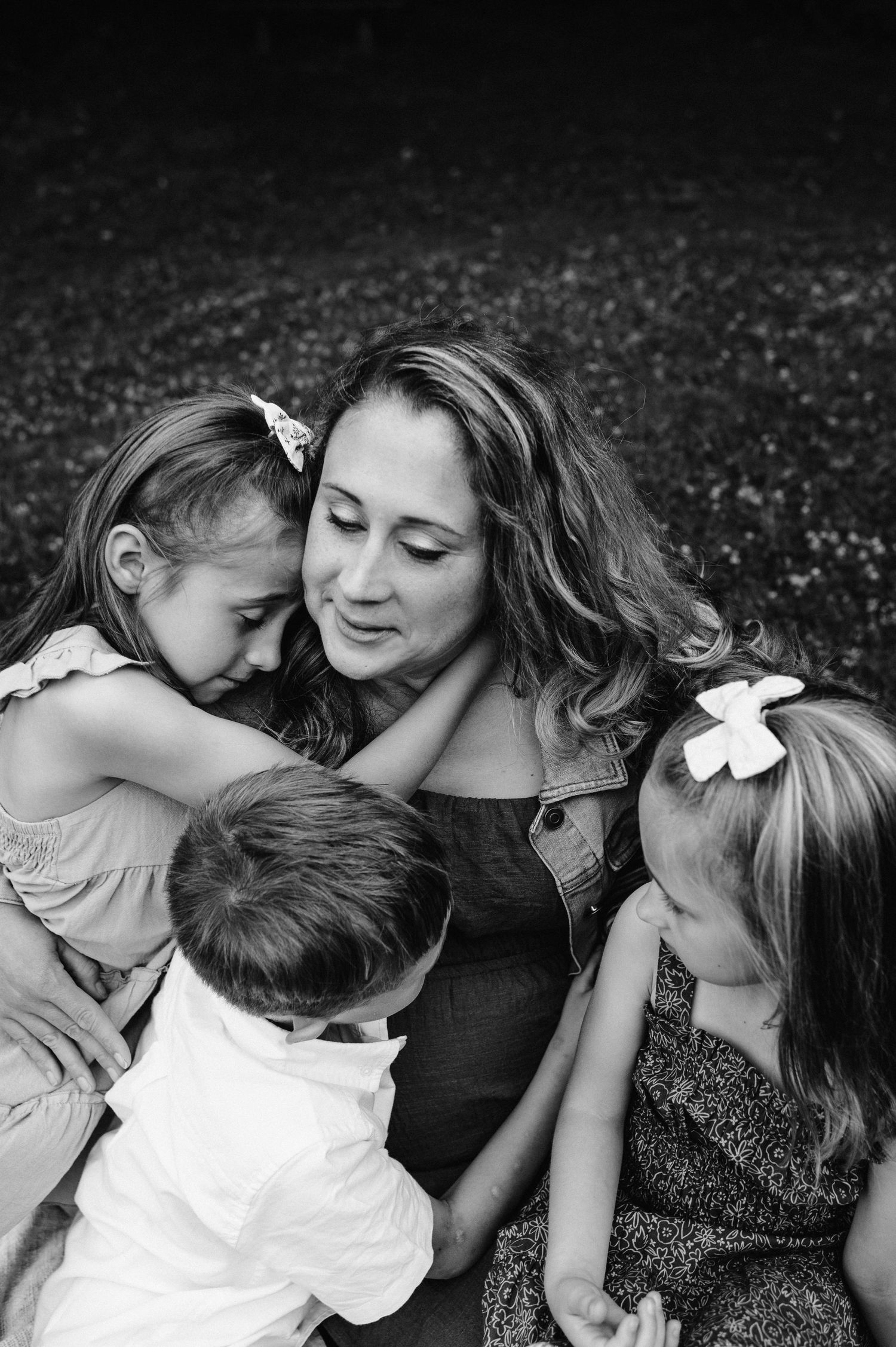 An intimate black and white family portrait showing tender moments of connection while sitting together outdoors.