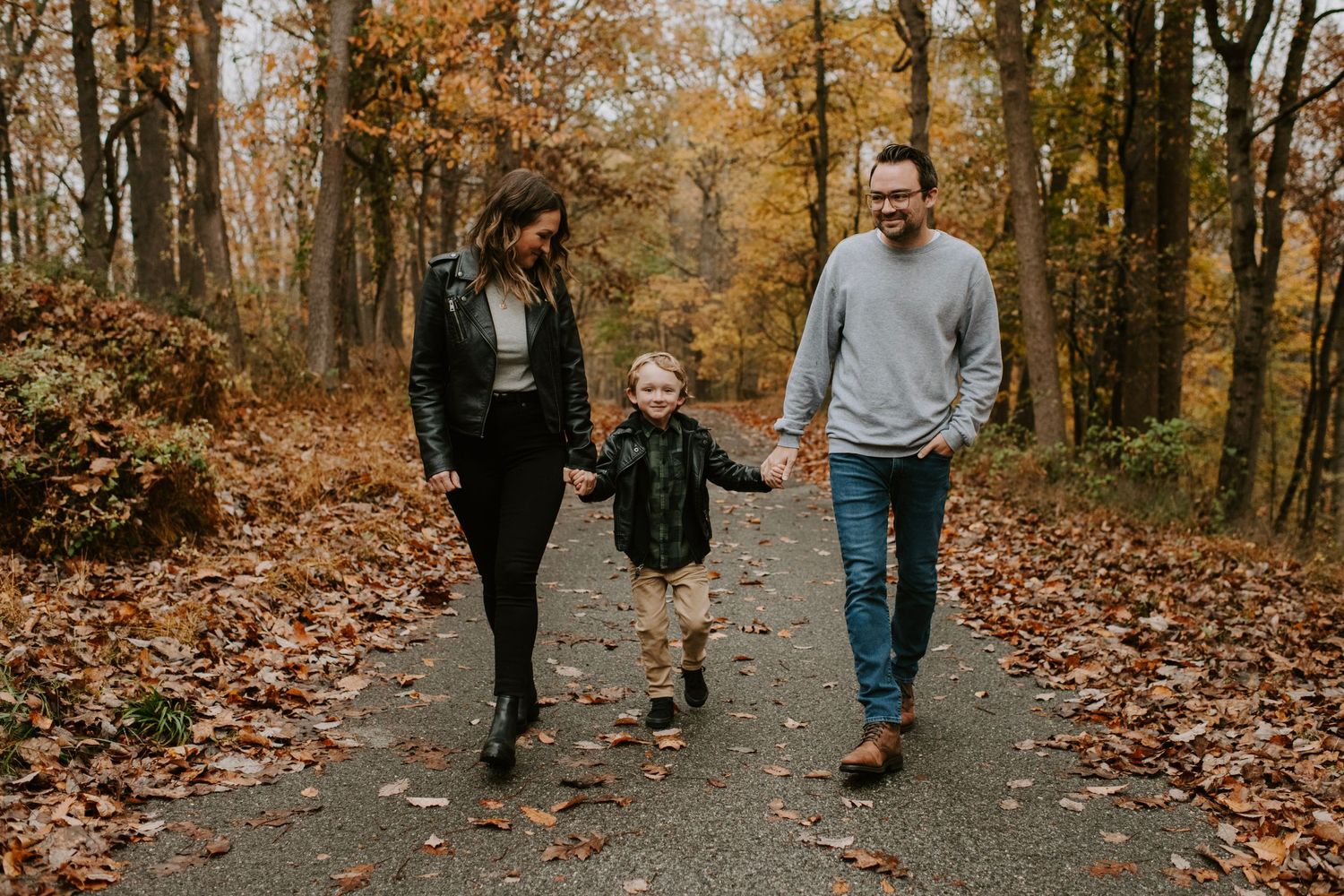 A family walks together on a leaf-covered path during autumn.