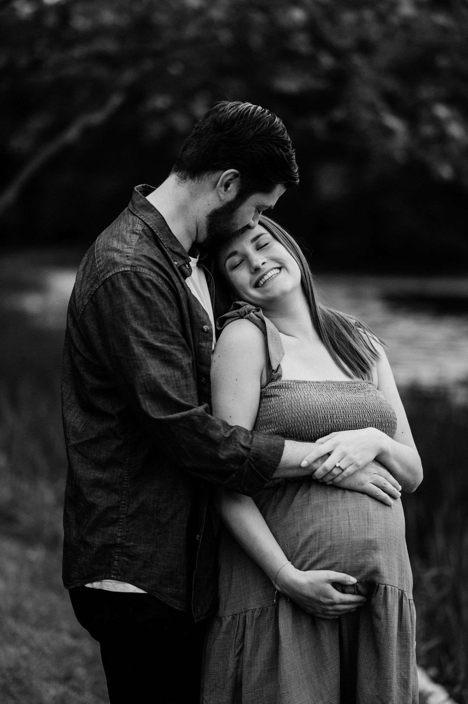 An intimate black and white moment between expectant parents in nature.
