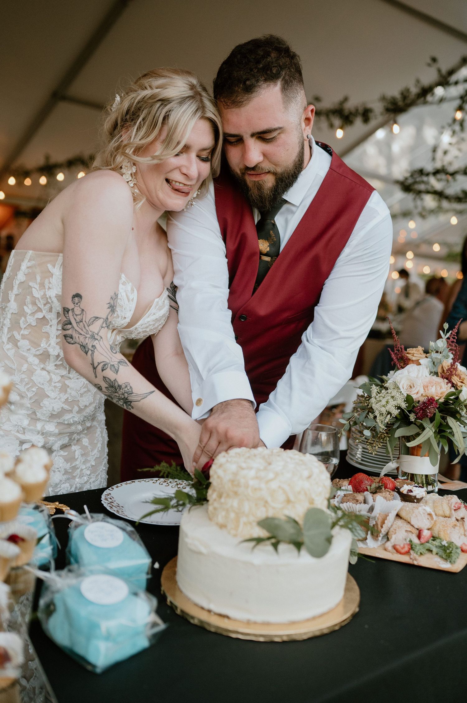 Newlyweds cut their white wedding cake together on a decorated table at their reception.
