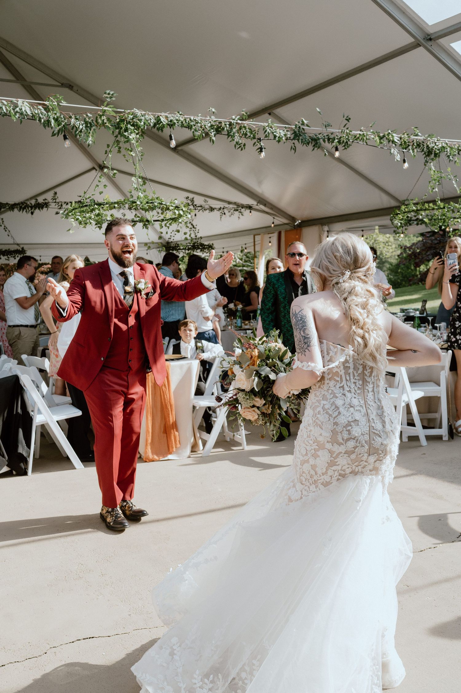 Wedding couple dancing under tent decorated with hanging greenery.