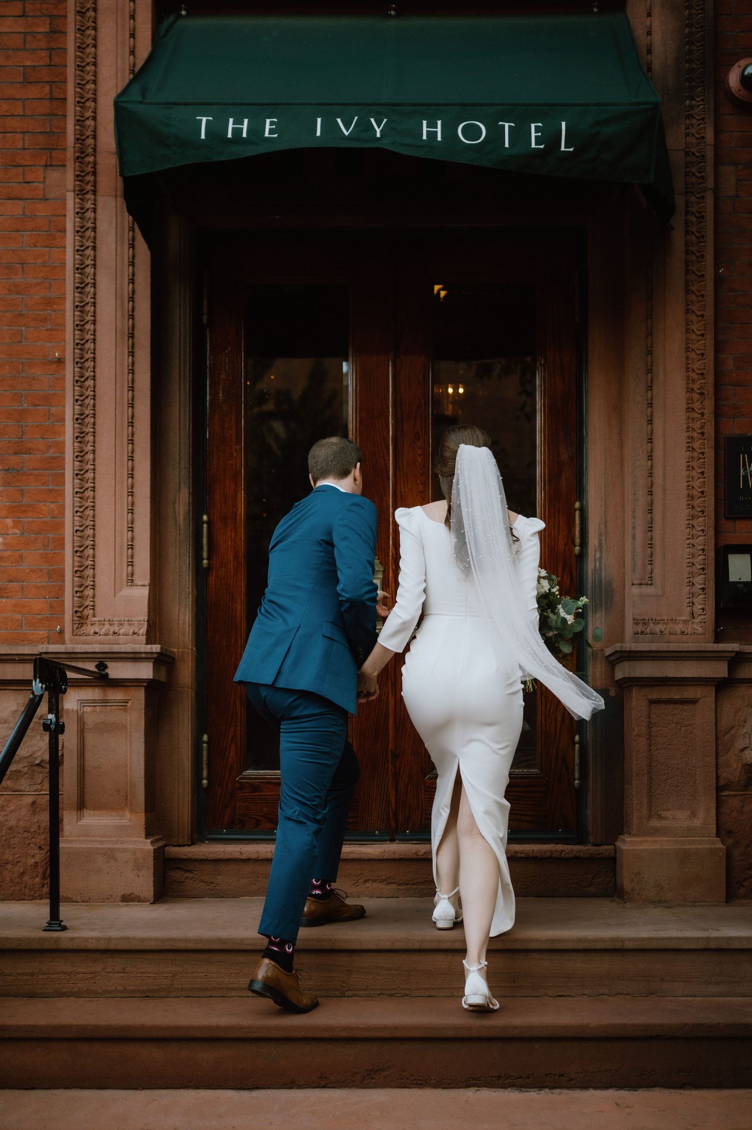 Couple entering The Ivy Hotel in elegant white dress and navy suit.