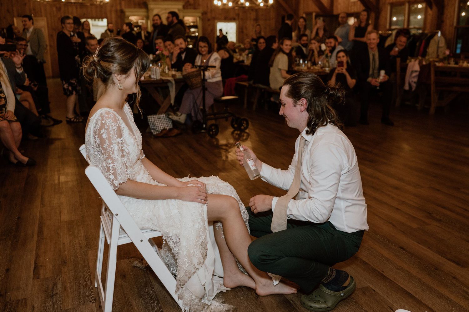 Intimate moment during wedding garter tradition with bride seated on white chair.