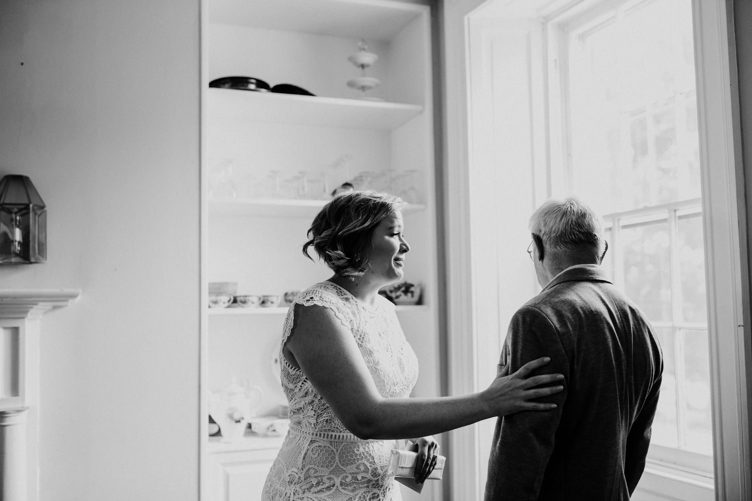 A black and white photo showing a tender moment between two people near a window.