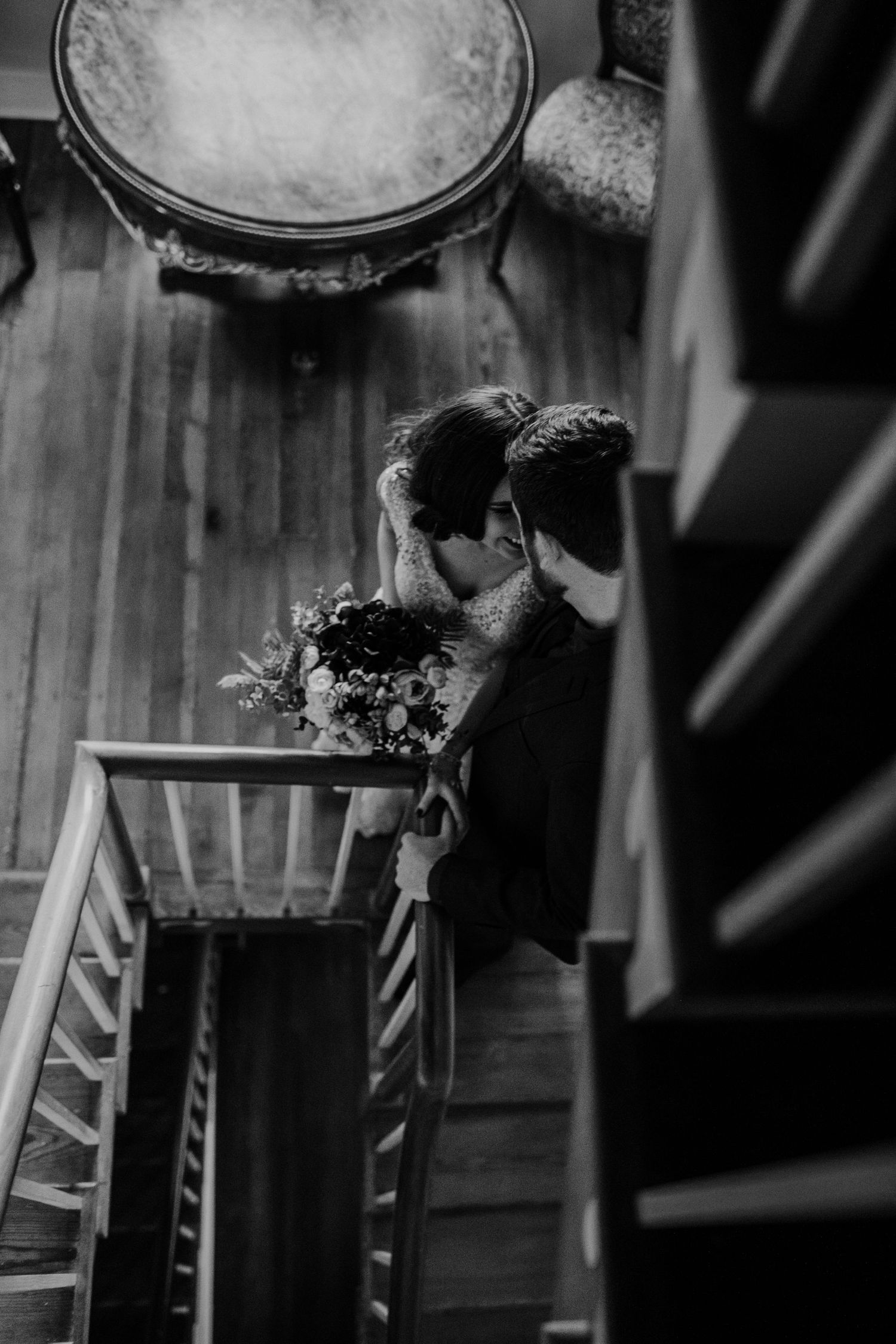 Black and white image of a couple on wooden stairs with flowers.