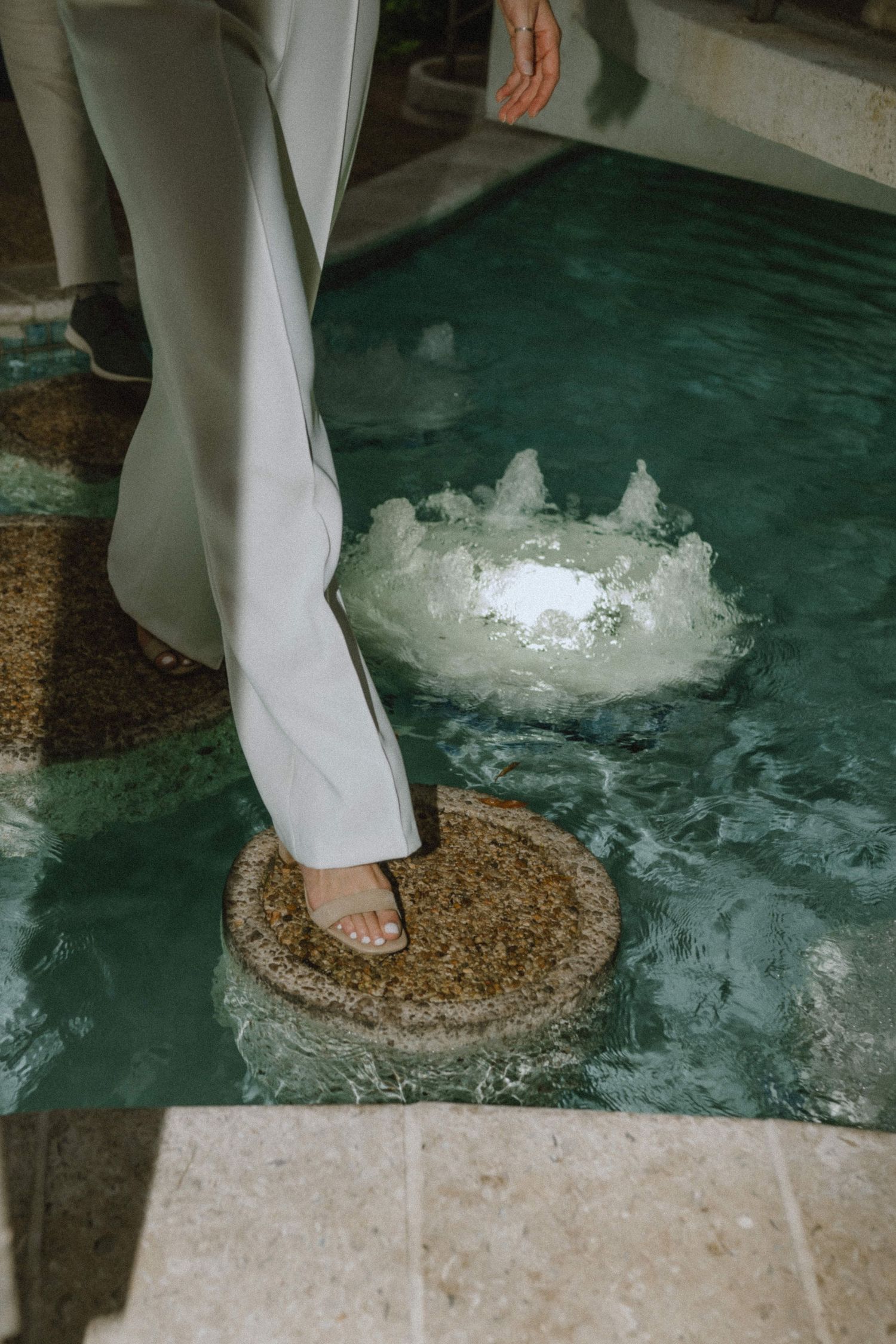 A person's feet standing on a circular stepping stone in a decorative pool with water features.