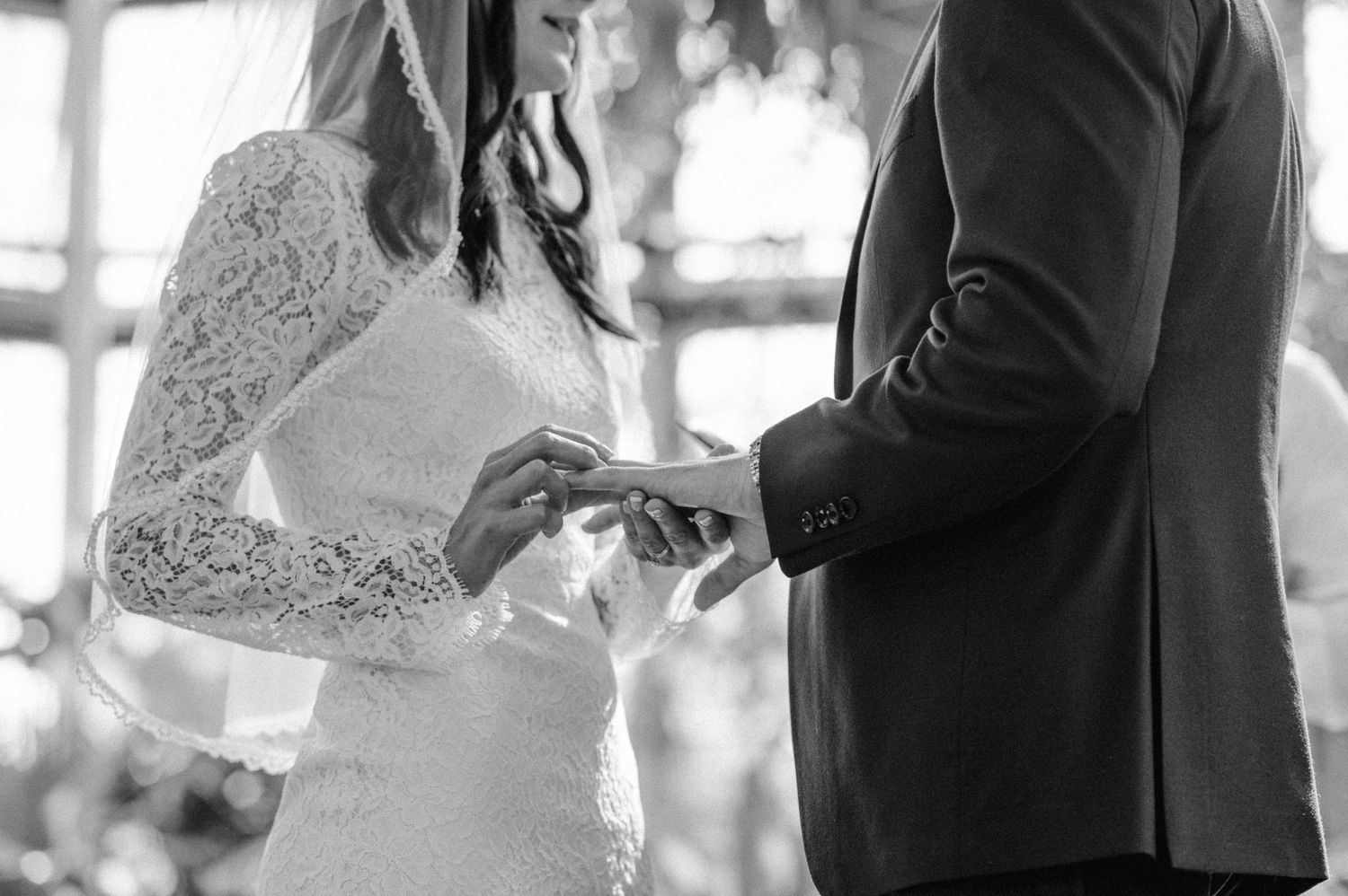 Close-up black and white photo of couple exchanging wedding rings during intimate ceremony.