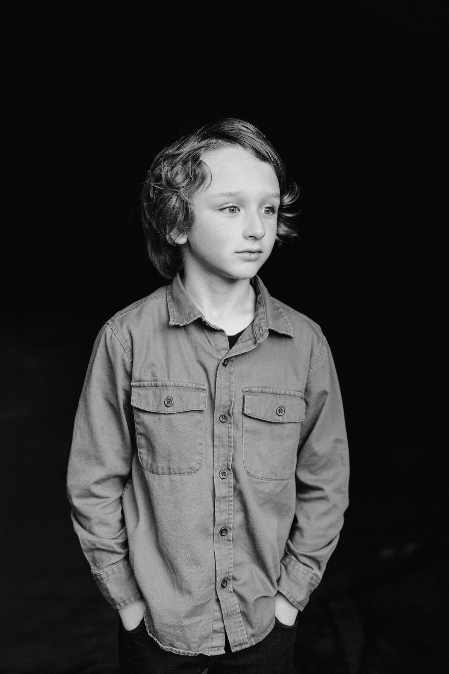 Dramatic black and white portrait of a youth in casual attire against dark background.
