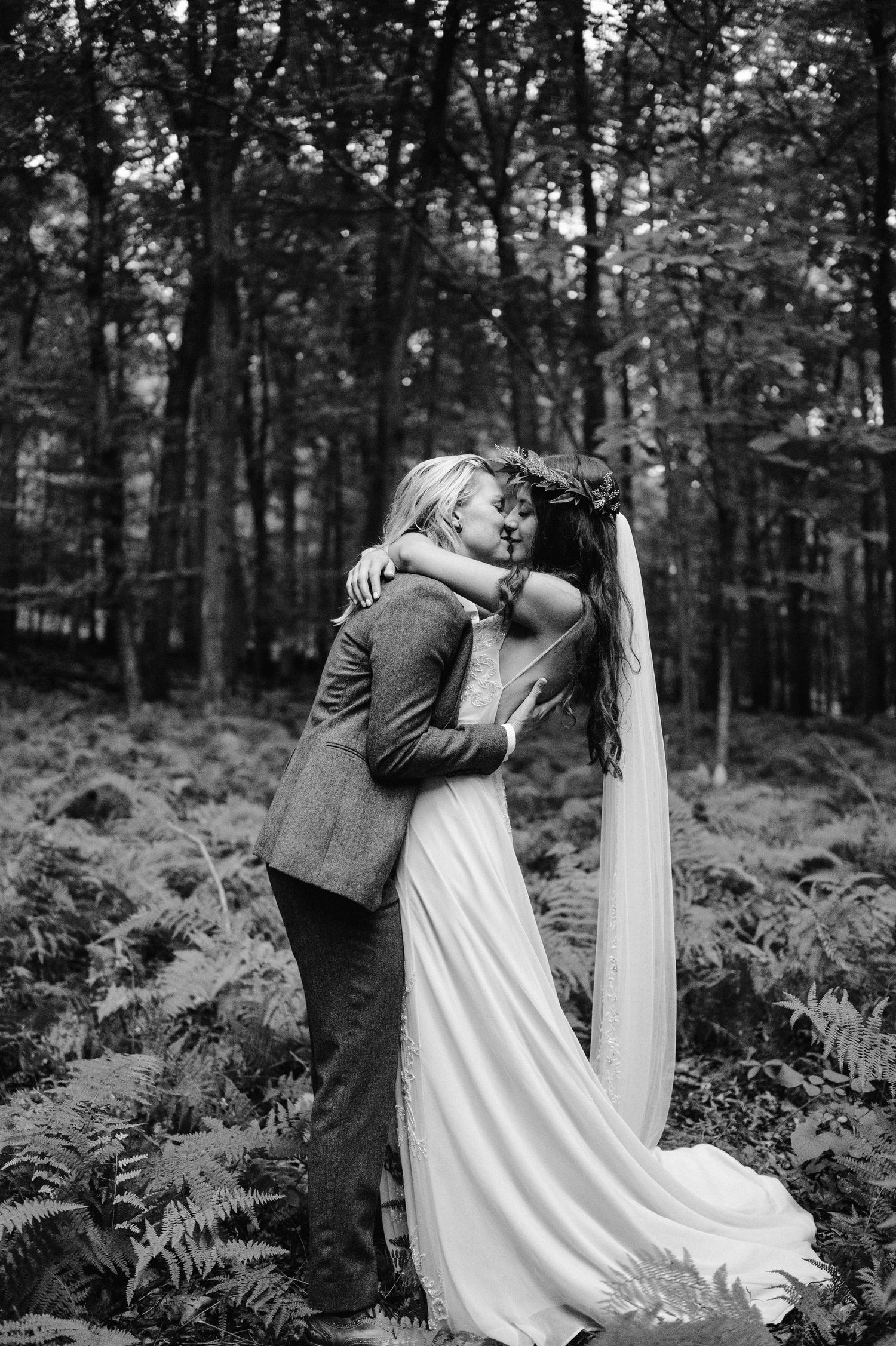 An intimate black and white wedding portrait capturing an embrace in a fern-filled forest.