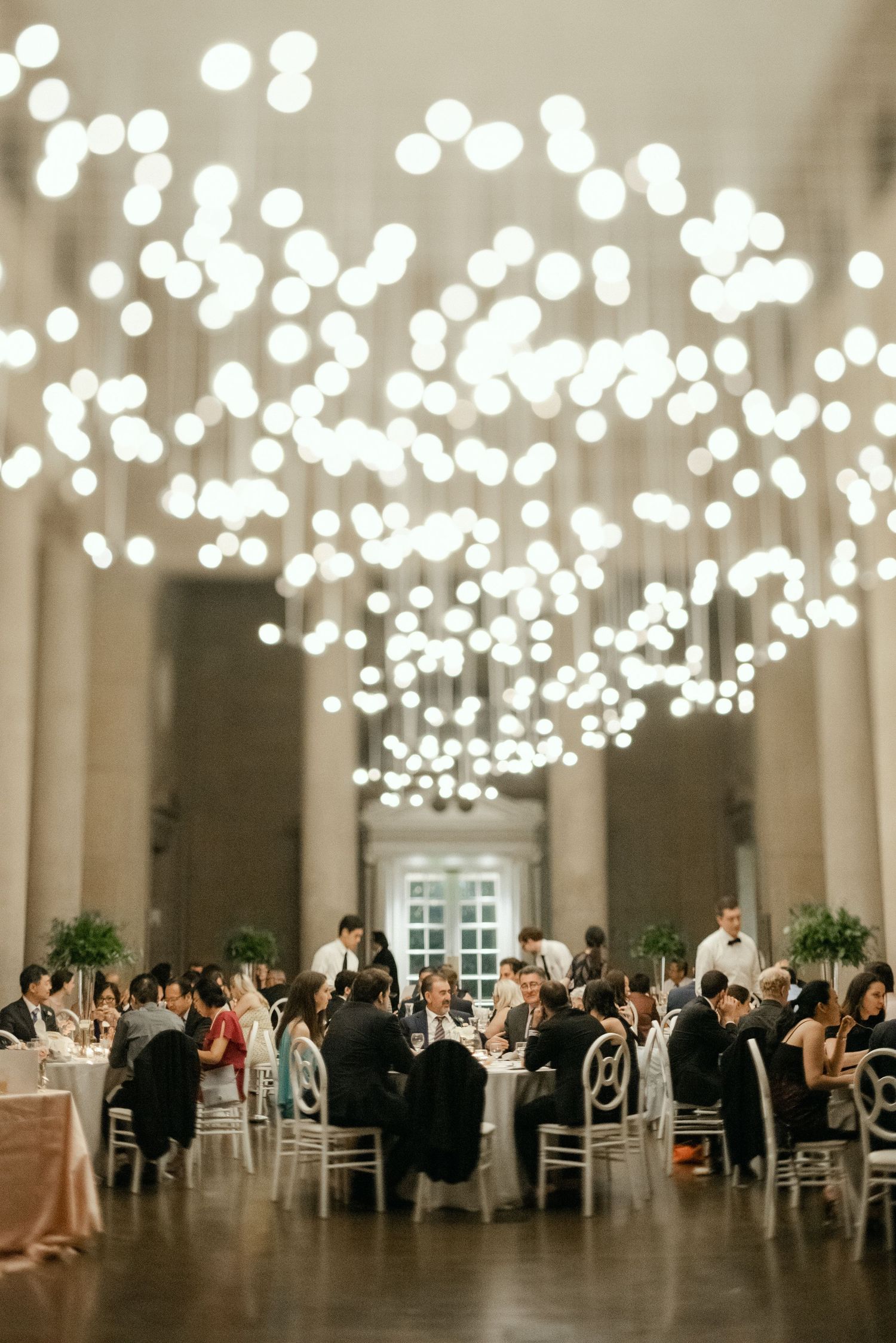 Grand ballroom filled with wedding guests under a canopy of glowing pendant lights.