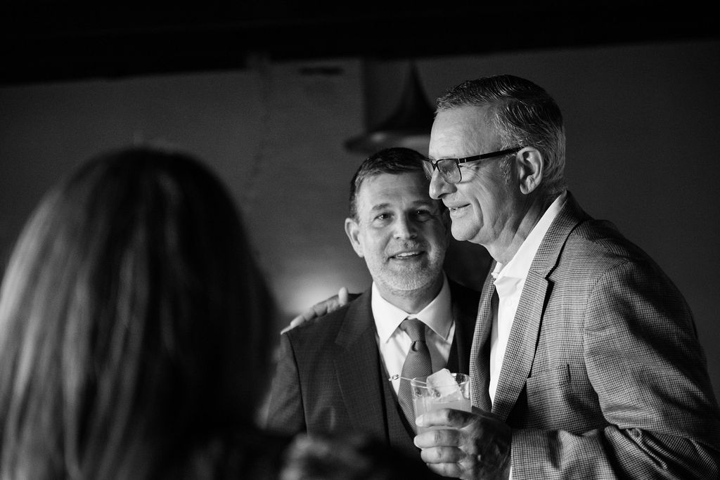 Black and white candid photo of guests sharing a laugh at an evening event.