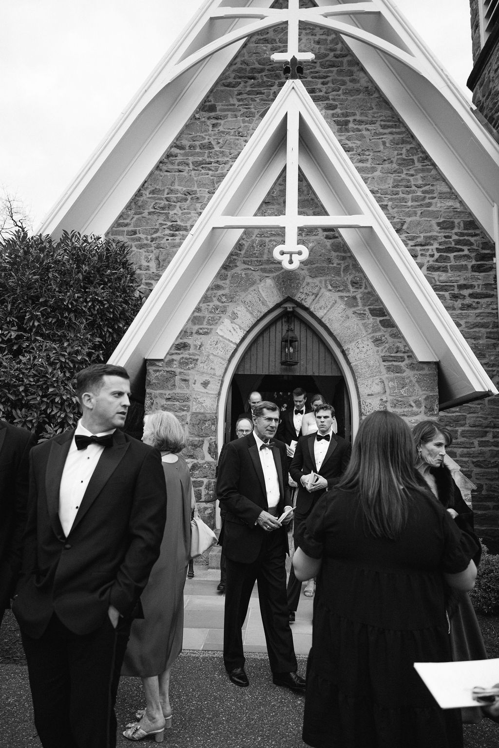 Wedding party gathered outside a stone church with gothic architecture and white trim details.