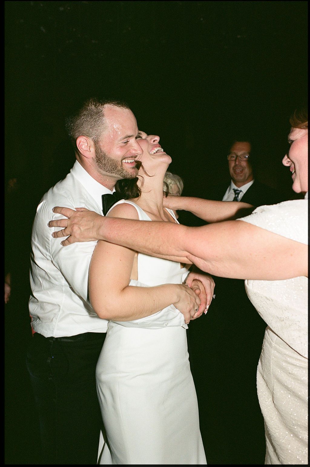 A couple in white attire dancing together during what appears to be a wedding reception.