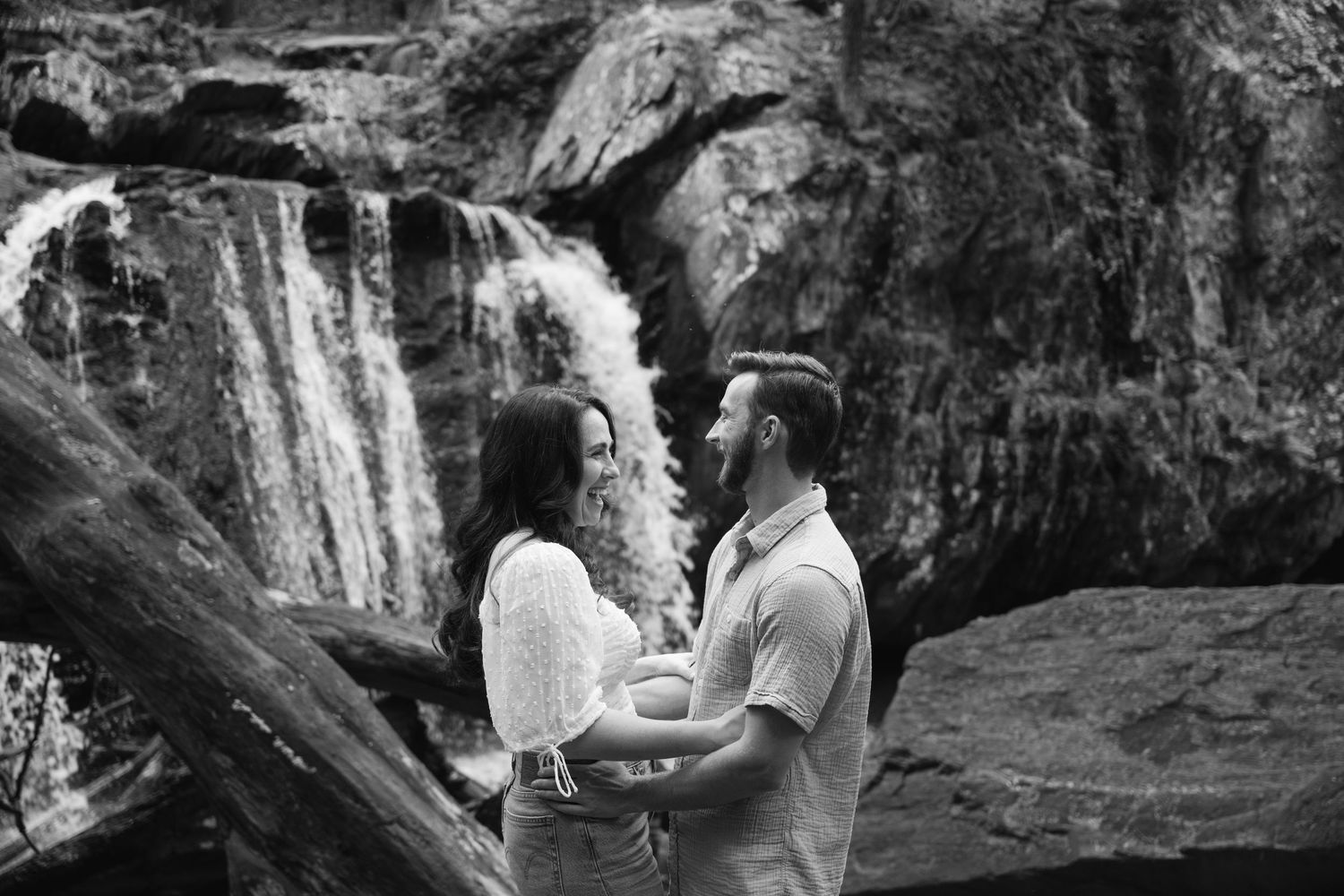 A scenic waterfall cascades down rocky cliffs surrounded by lush forest in a natural setting.