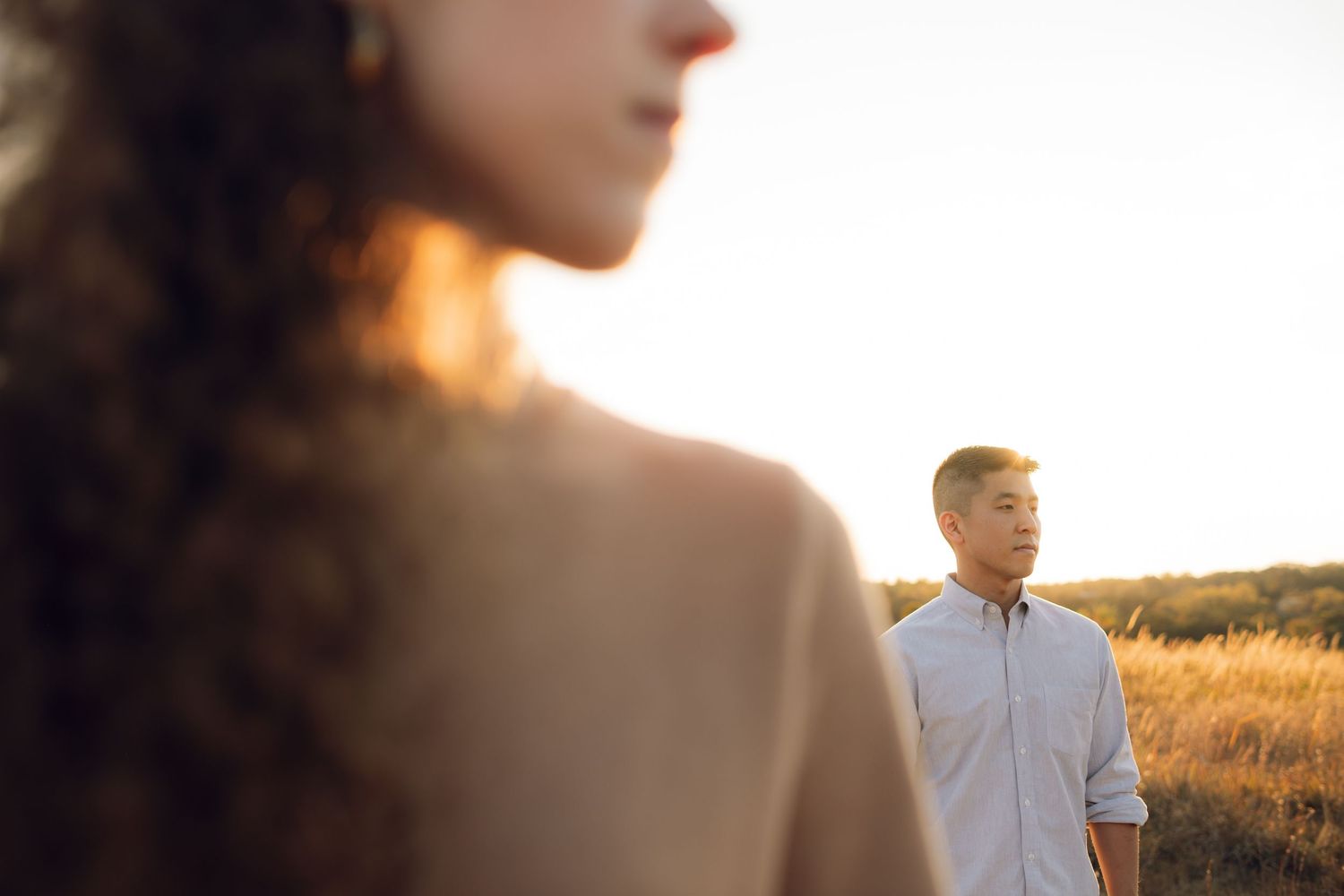 A couple walks through a golden field at sunset creating silhouettes against the warm sky.