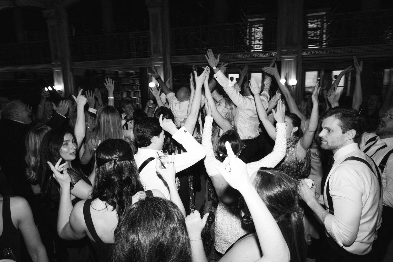 Black and white photo of a crowded dance floor with people raising their hands in celebration.