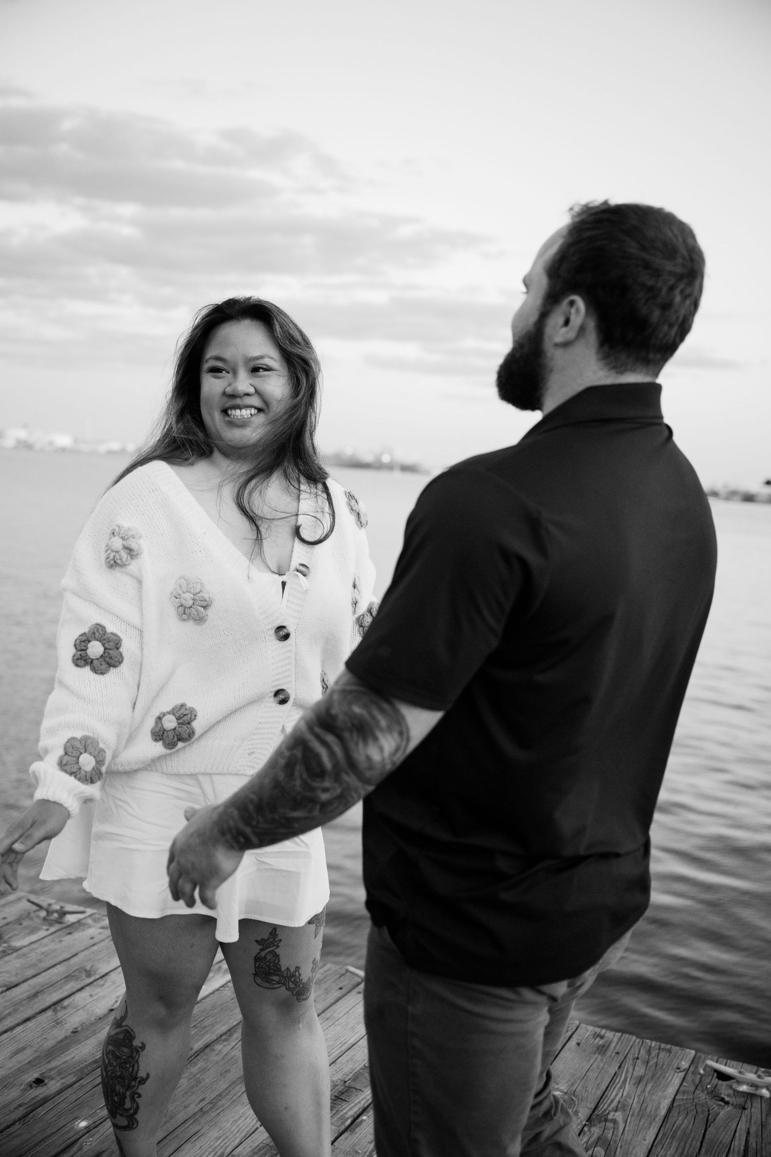 A romantic couple enjoys a playful moment together on a wooden dock by the waterfront at sunset.