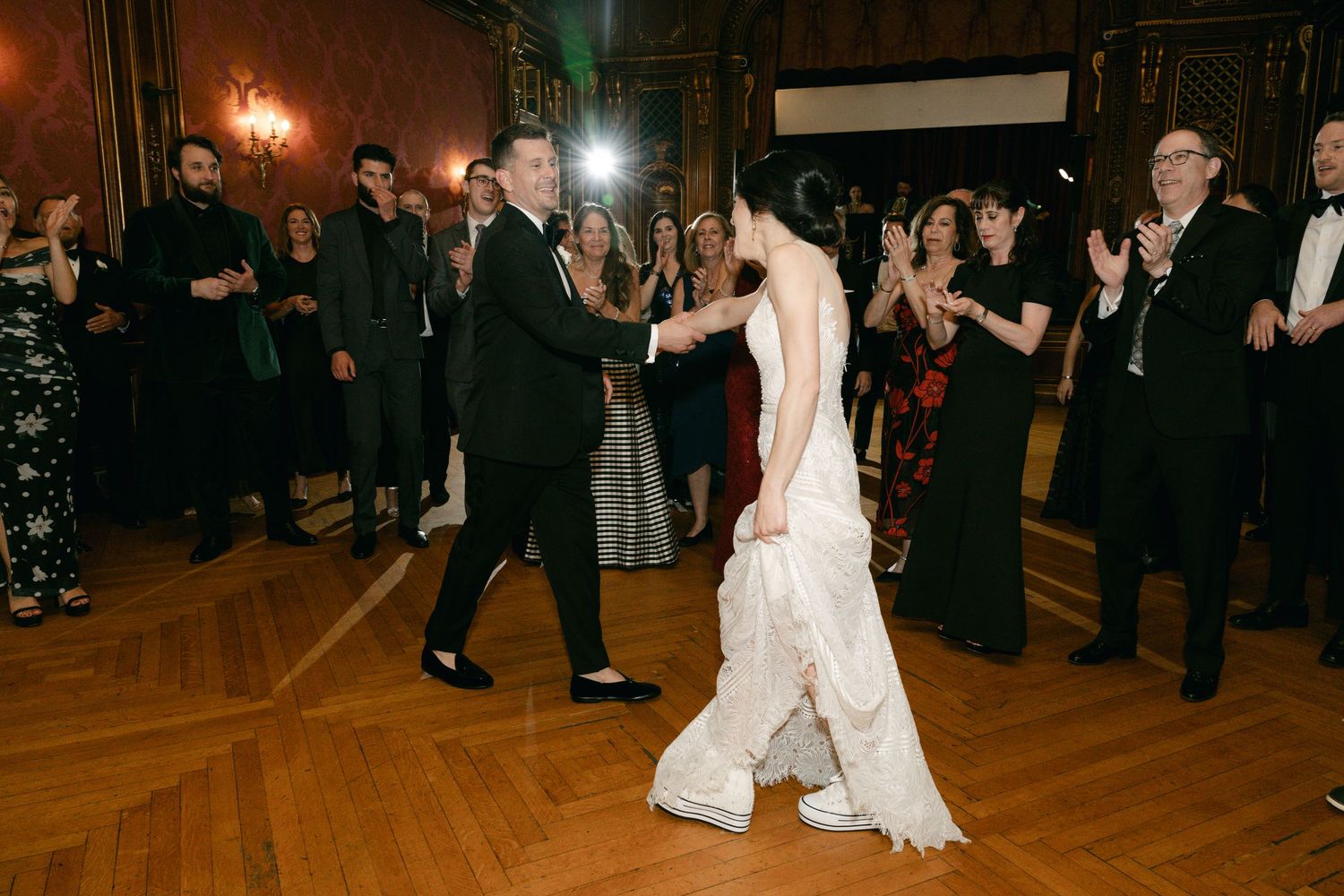 Couple dancing at their wedding reception in a grand ballroom with wooden floors.