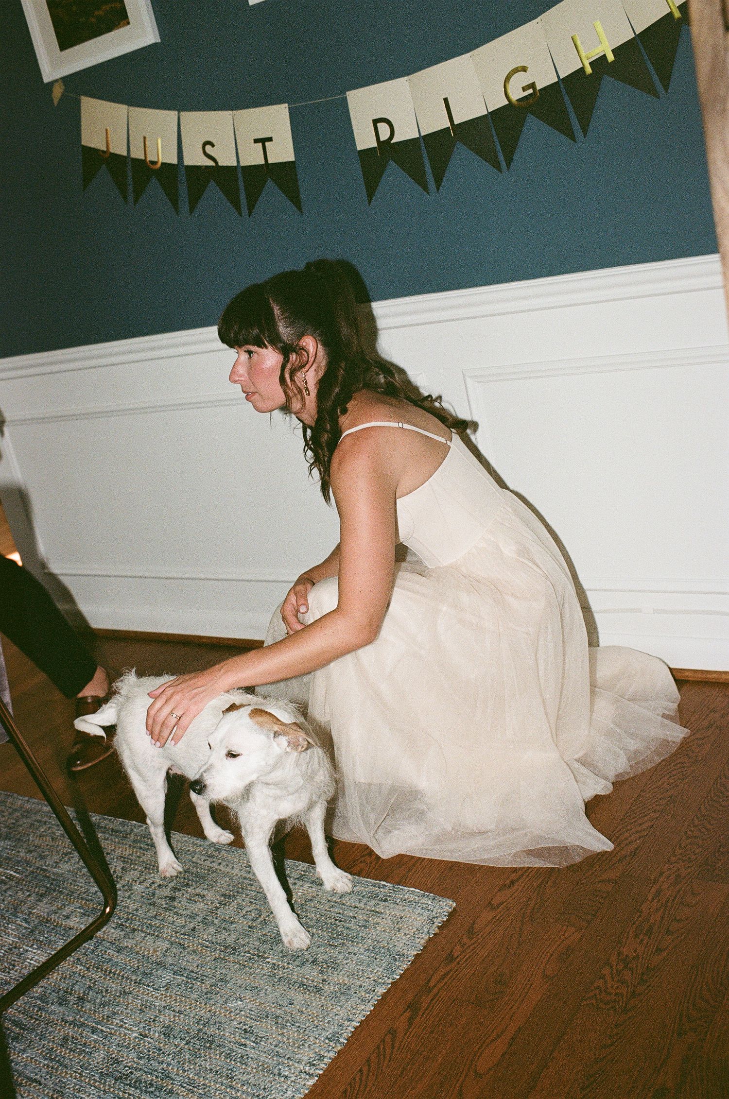 A woman in a light-colored dress pets a white dog during a celebration with a banner hanging overhead.