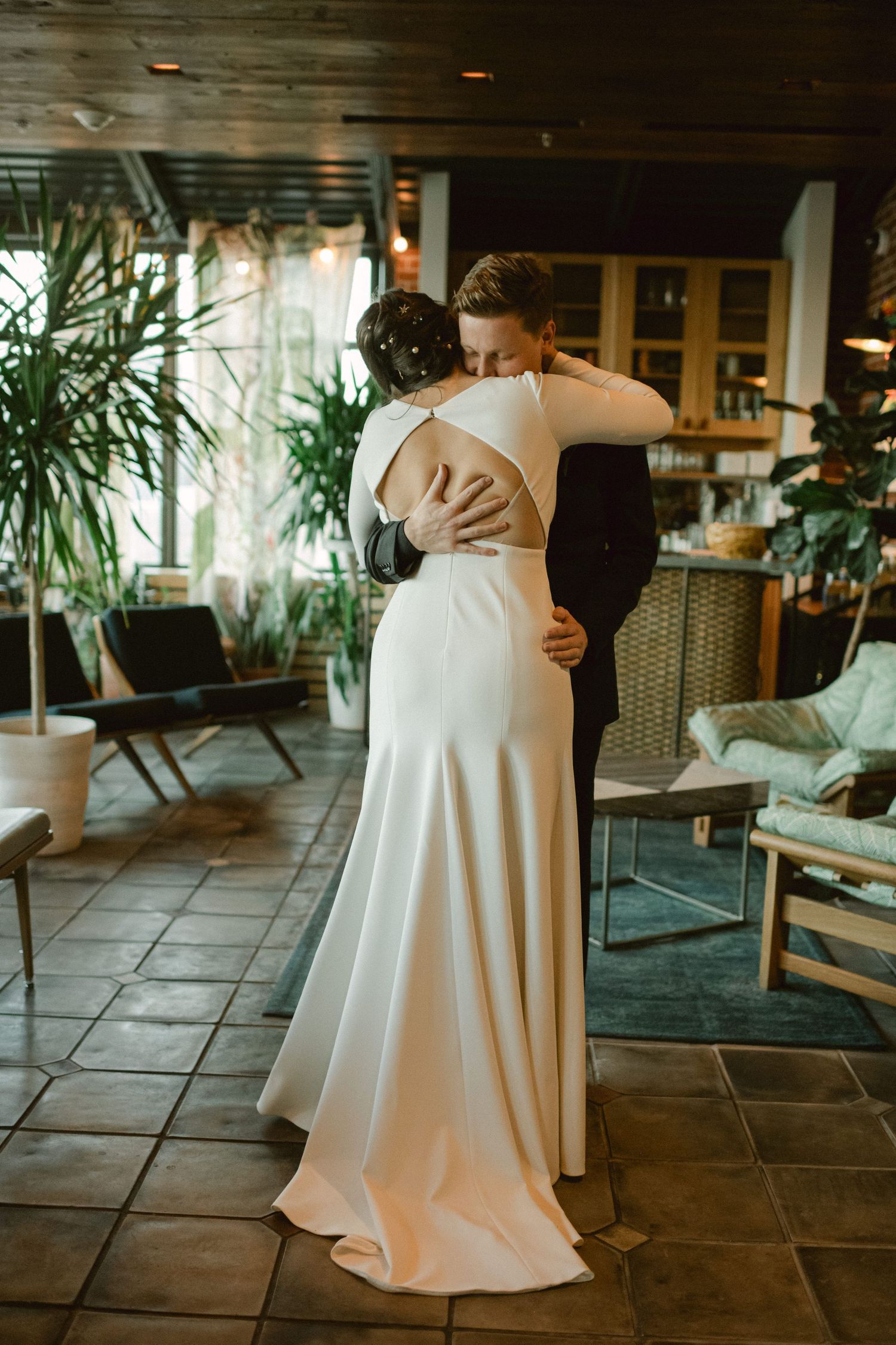 Intimate embrace between couple during wedding ceremony with indoor plants in background.