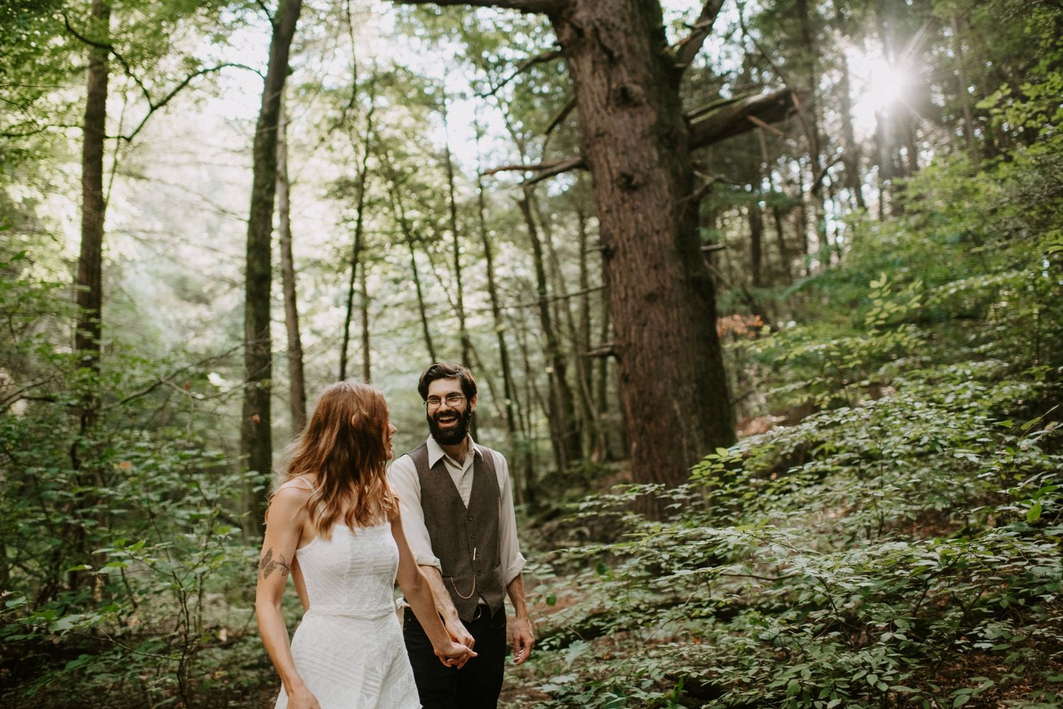 Couple shares tender moment in sun-dappled green forest setting.