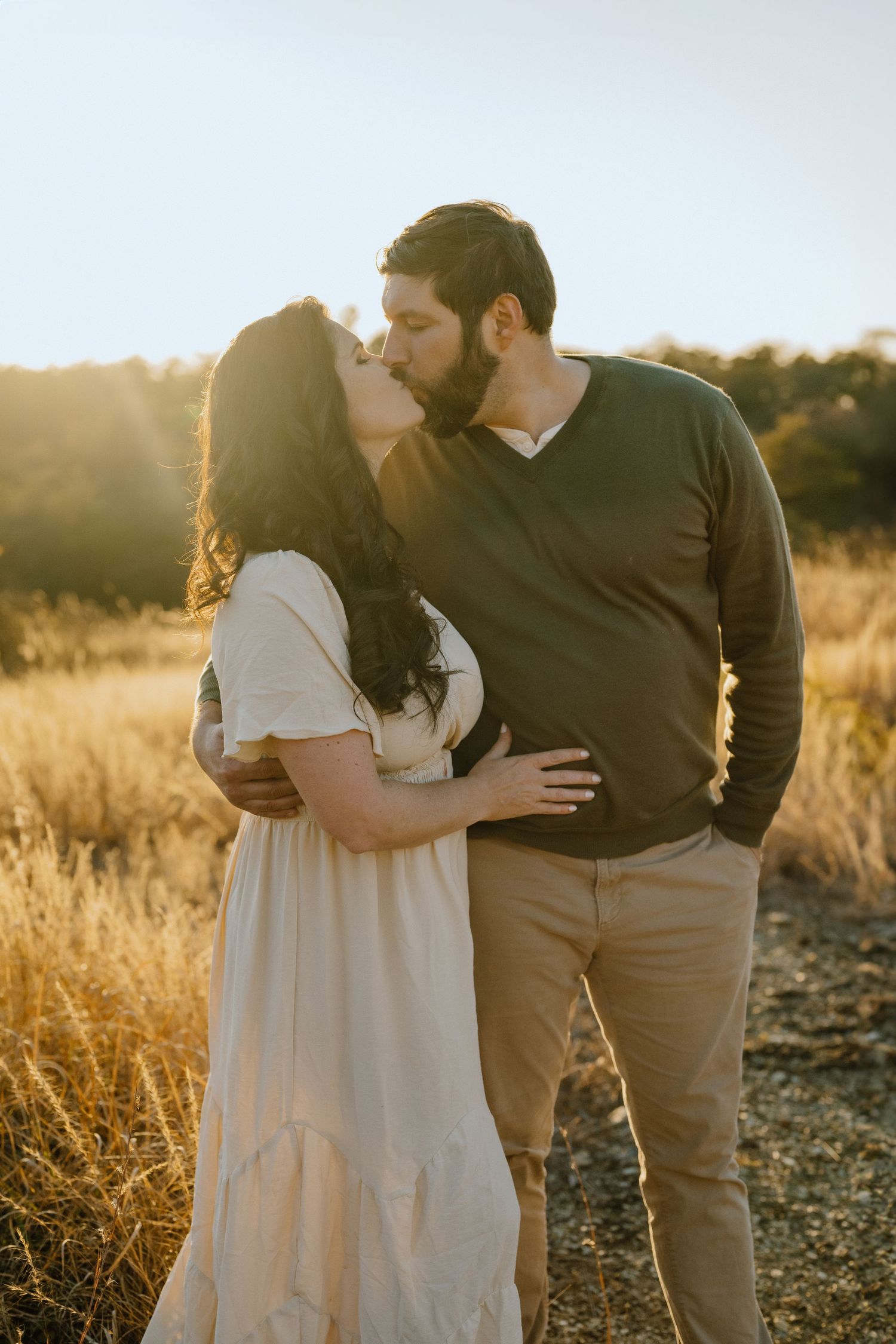 A couple shares a tender kiss in a sun-drenched field of golden grass at sunset.