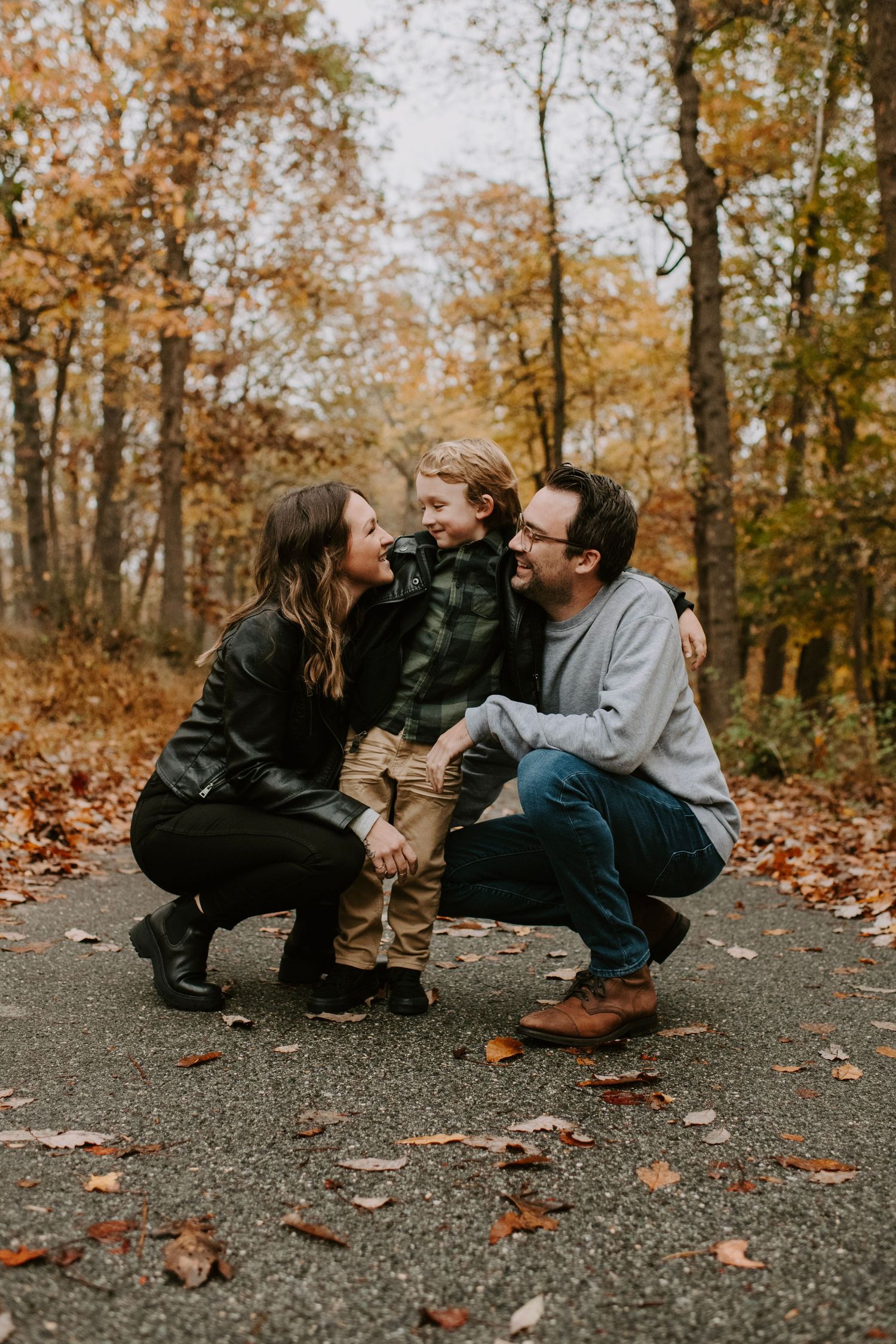 A sweet family moment captured on an autumn path surrounded by fallen leaves.