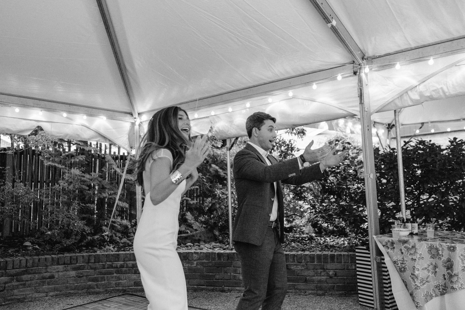 Couple dancing energetically under white tent at outdoor wedding reception.
