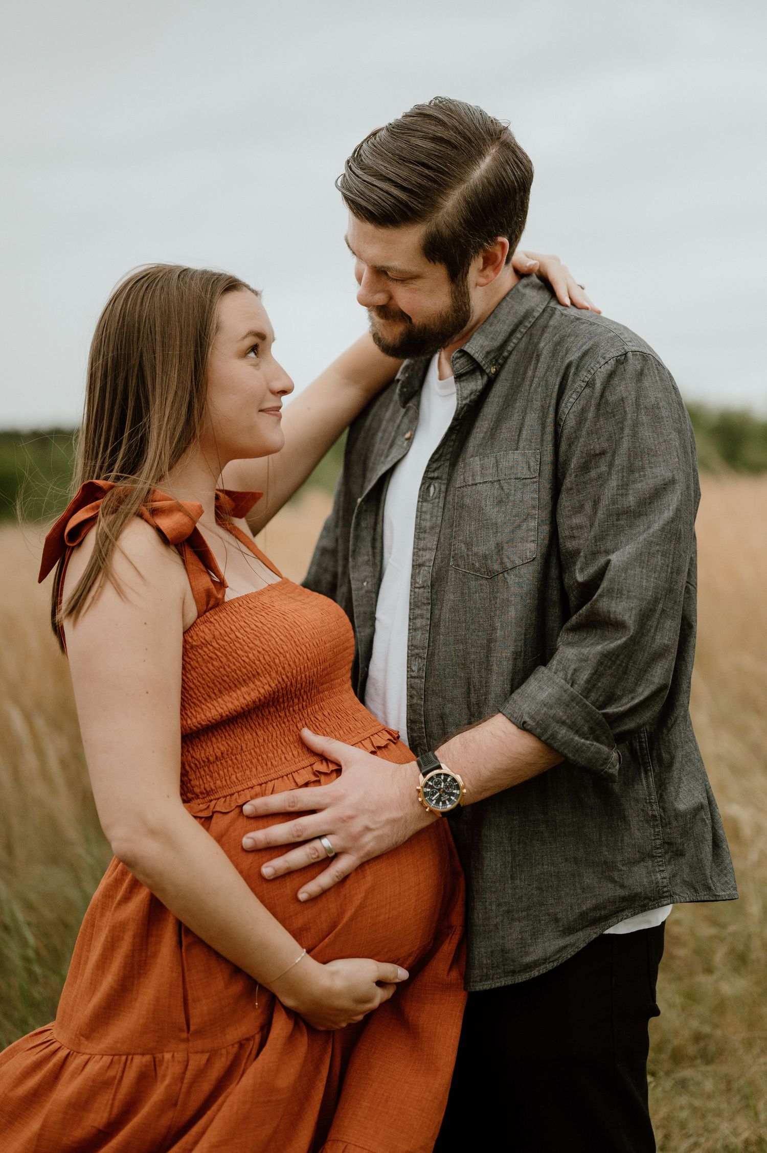Expecting couple sharing tender moment in field during sunset photoshoot.