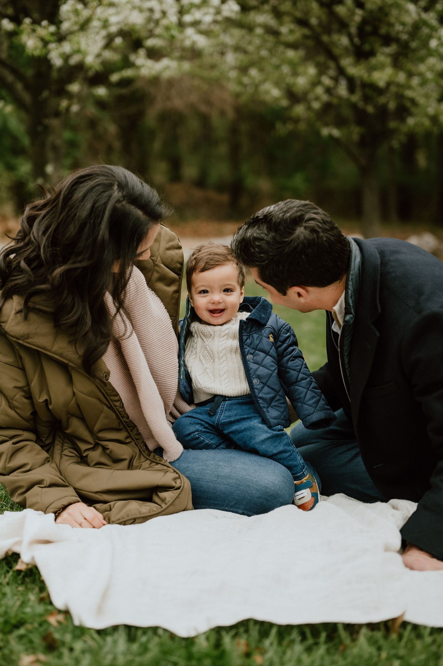 Candid family moment on white blanket with laughing toddler.