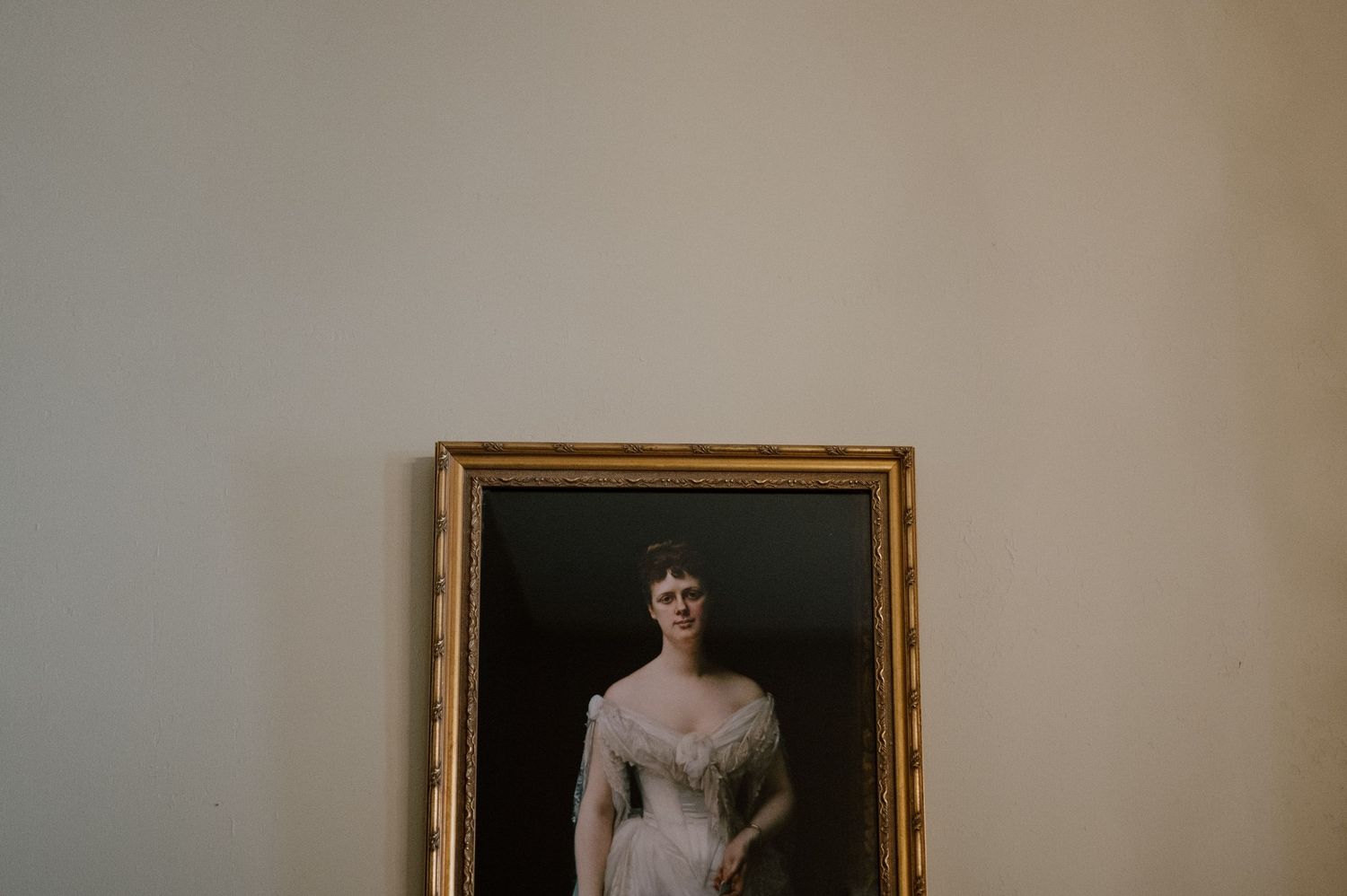 Gold-framed classical portrait painting hanging on a light colored wall.